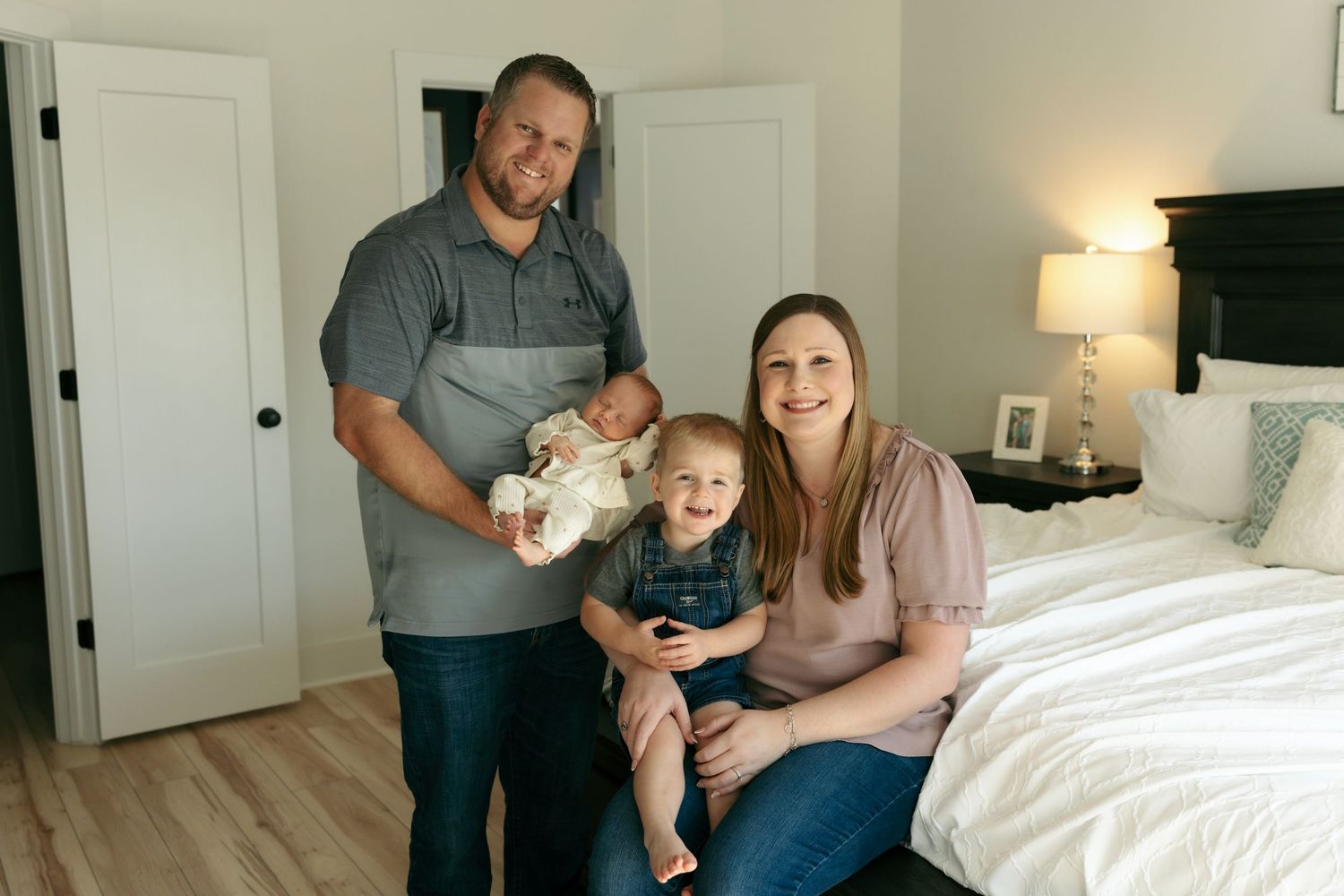 Family of four posing in bedroom with newborn baby and toddler son.