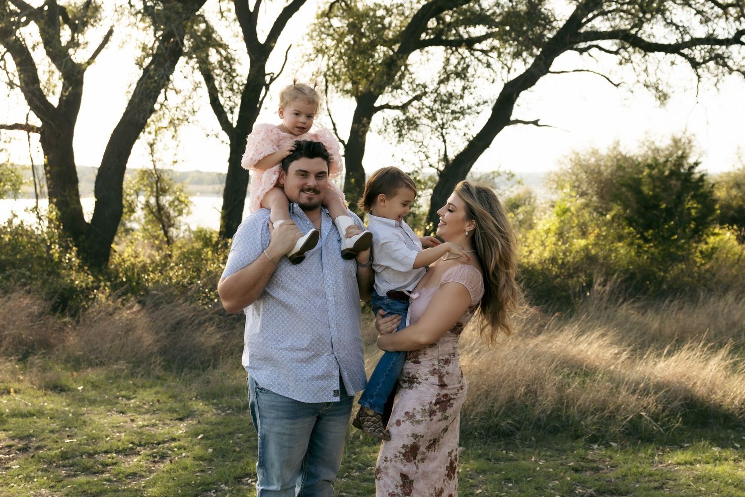 Happy family of four with two young children enjoying outdoor photo session at golden hour.