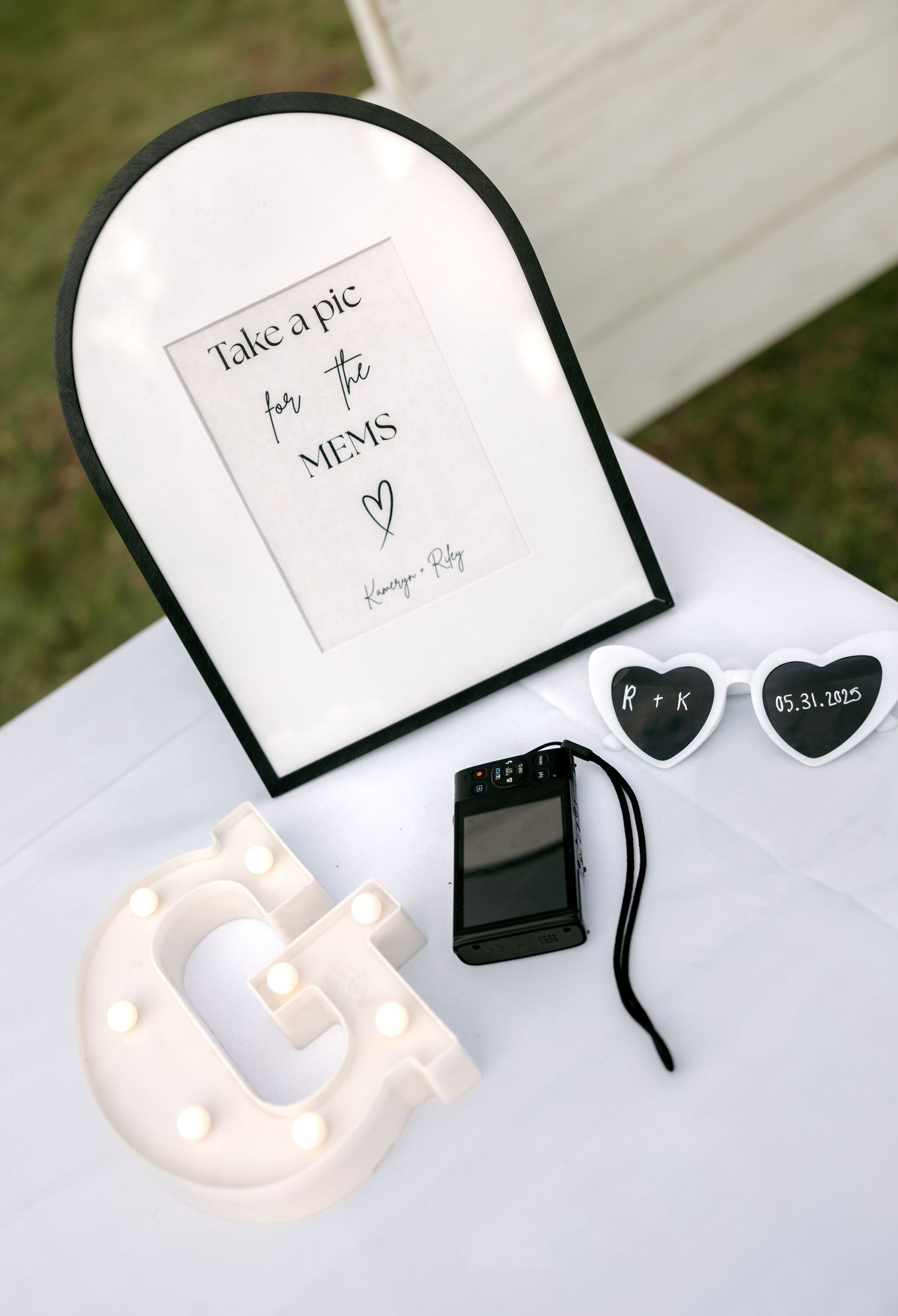 Wedding guest book table with framed sign, disposable camera, heart sunglasses, and marquee letter decoration.