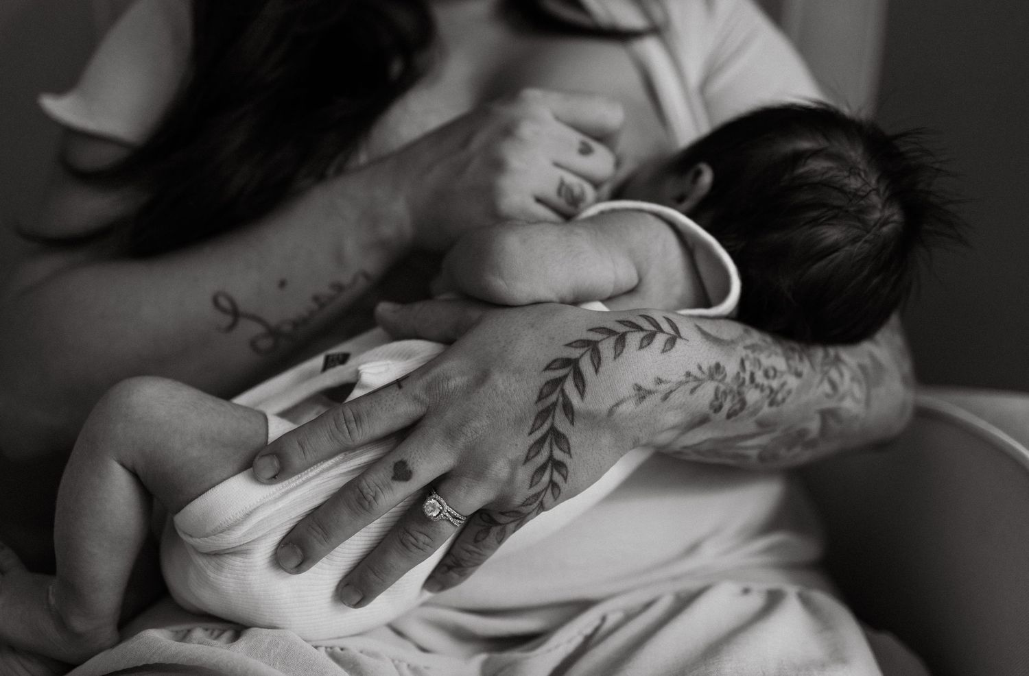Close-up black and white photo of tattooed hands cradling a sleeping newborn baby.