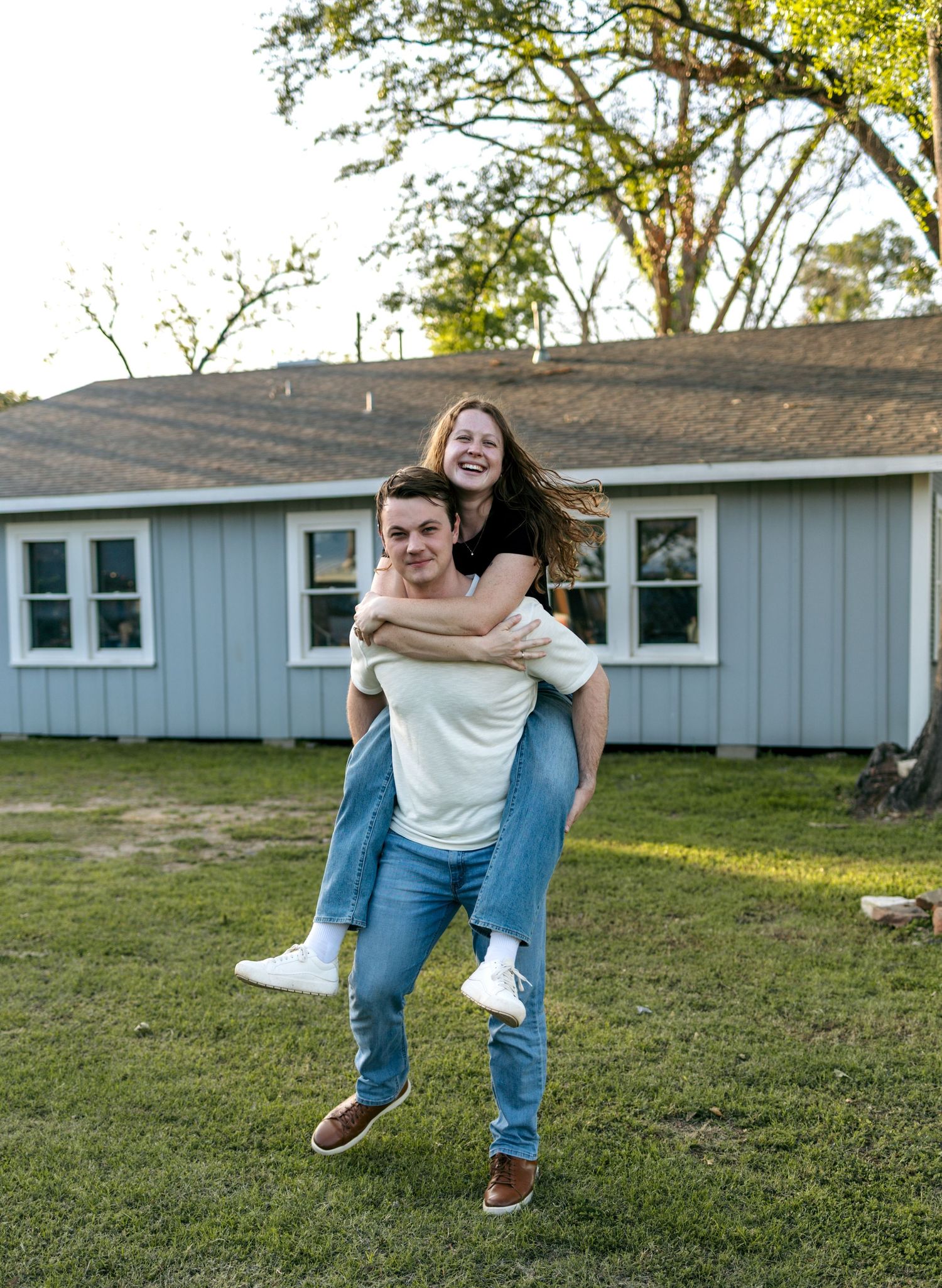 Young man giving smiling woman a piggyback ride in front yard.