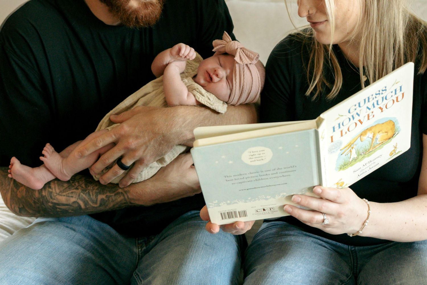 Parents reading a book to their newborn baby while sitting together on a couch.