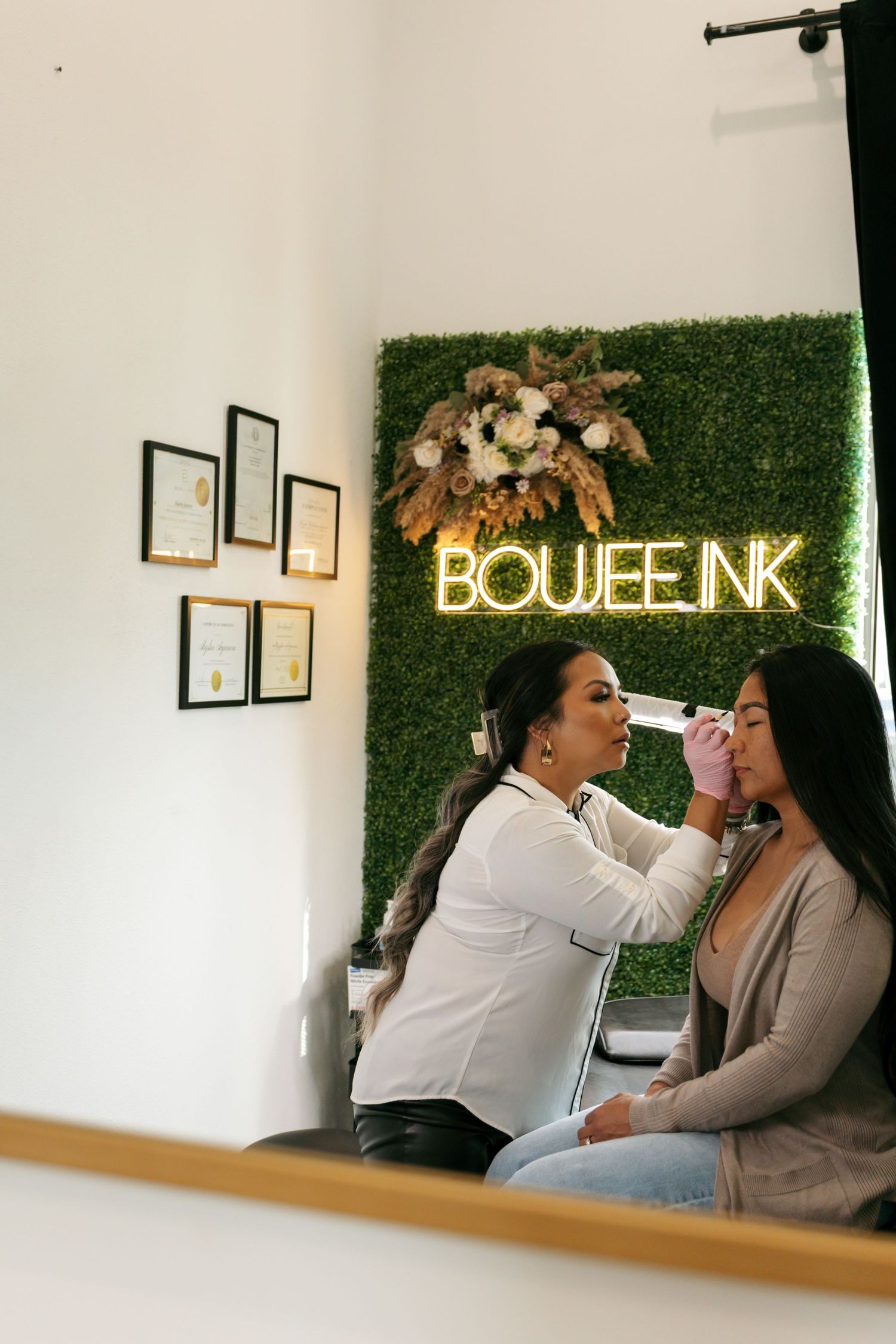 Beauty professional applying a cosmetic treatment to a seated client at Boujee Ink studio.