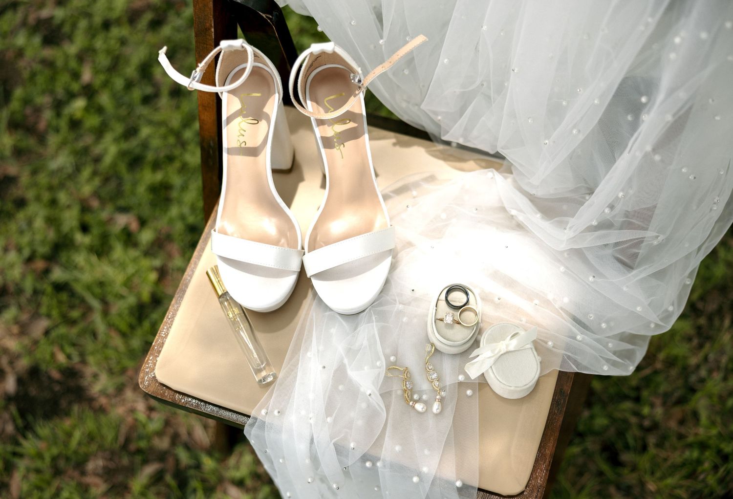 White bridal heels displayed on vintage suitcase with veil, perfume, and pearl accessories for wedding day.