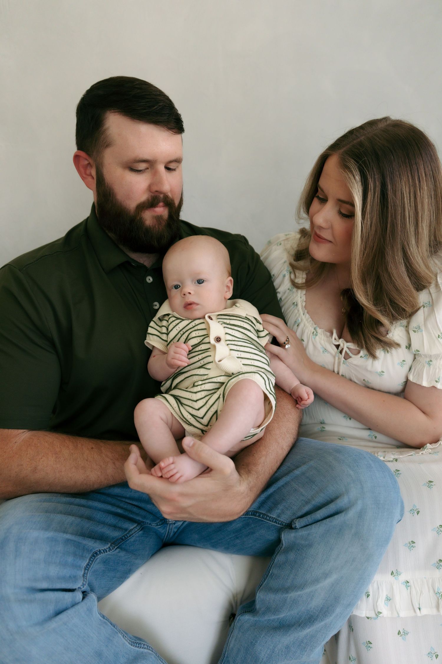 Parents in green and white outfits lovingly gazing at their alert newborn baby boy.
