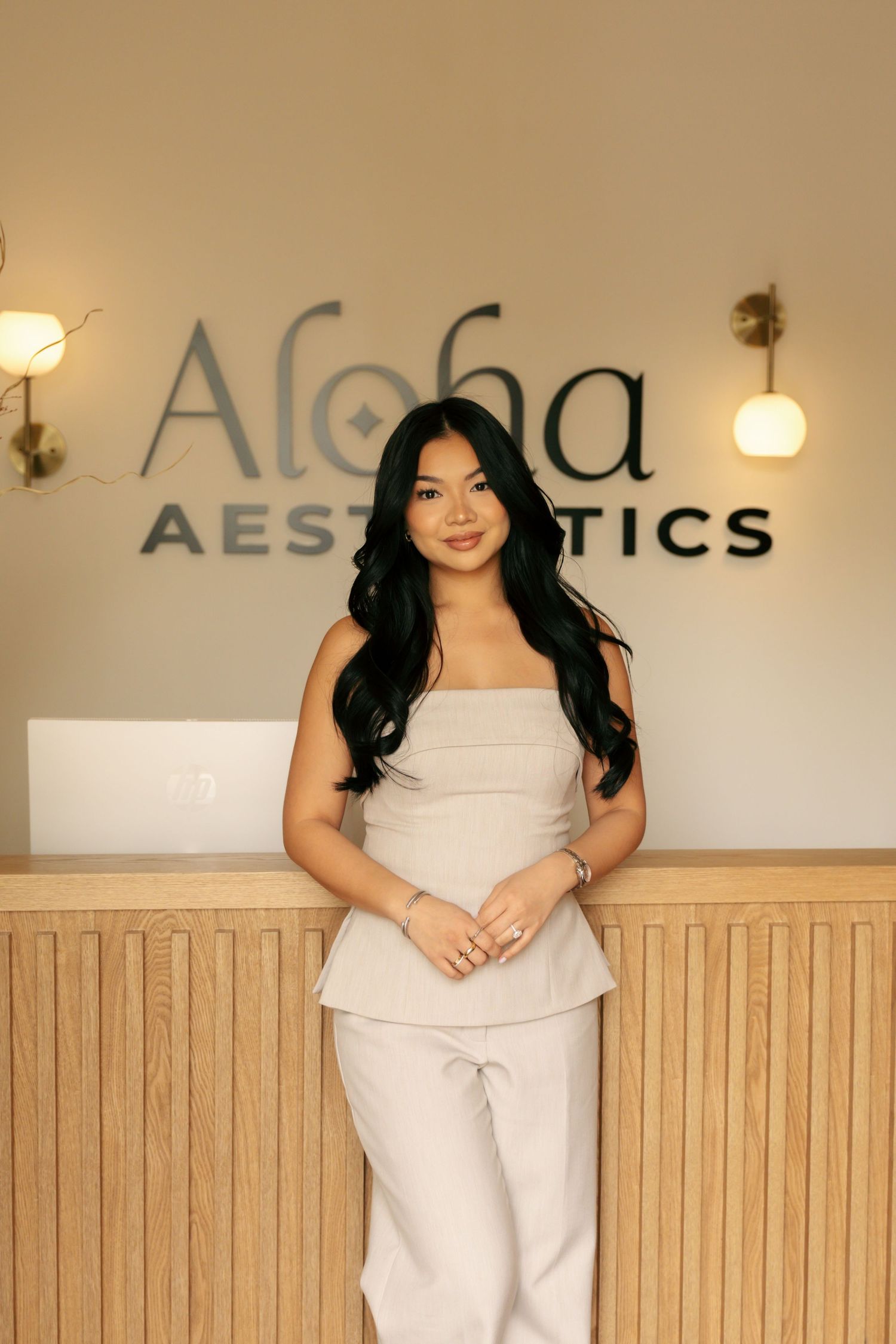 Young woman in neutral outfit standing confidently at the Aloha Aesthetics reception desk.