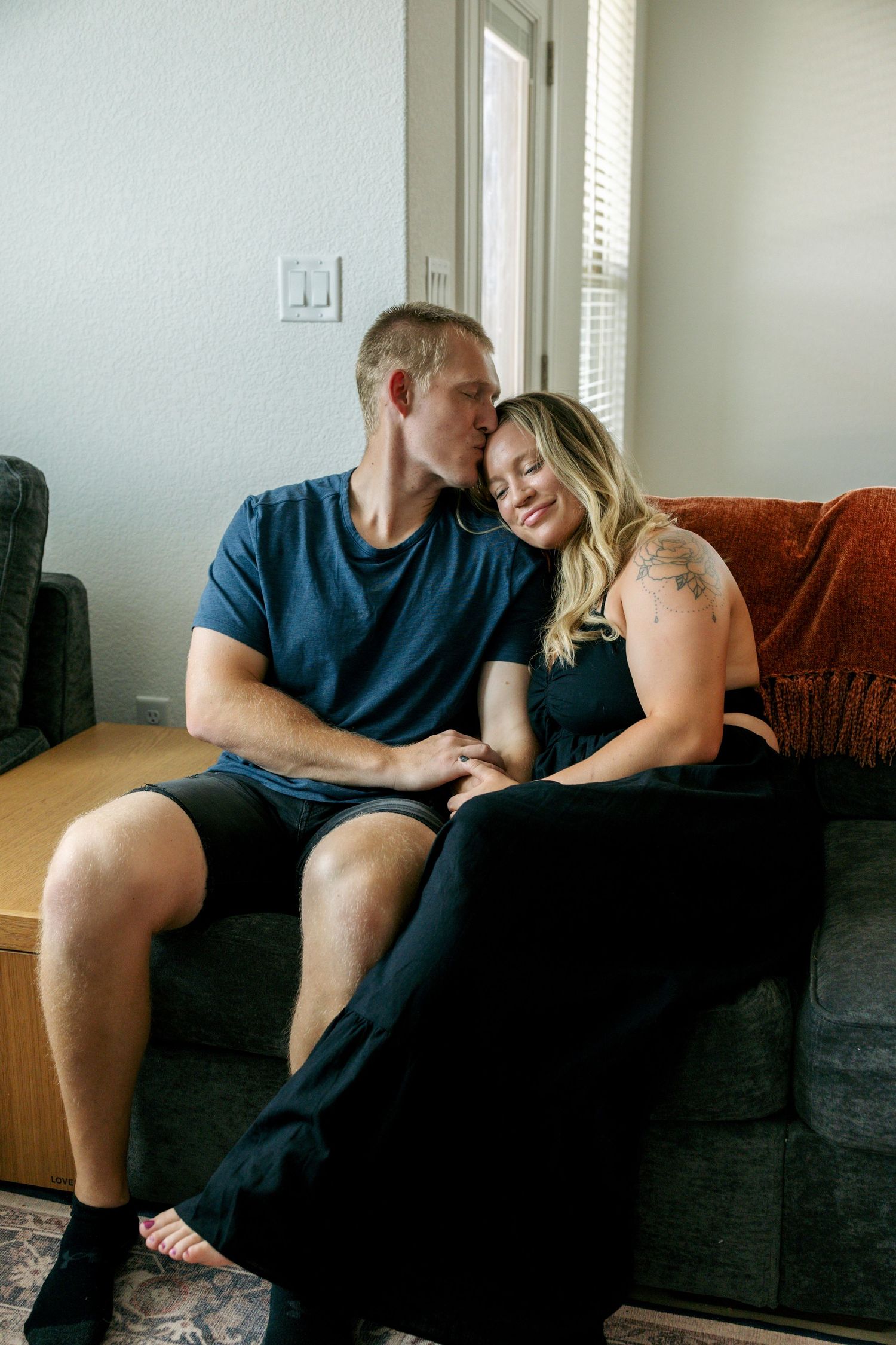 Couple sharing tender moment on couch, man kissing woman on forehead indoors.