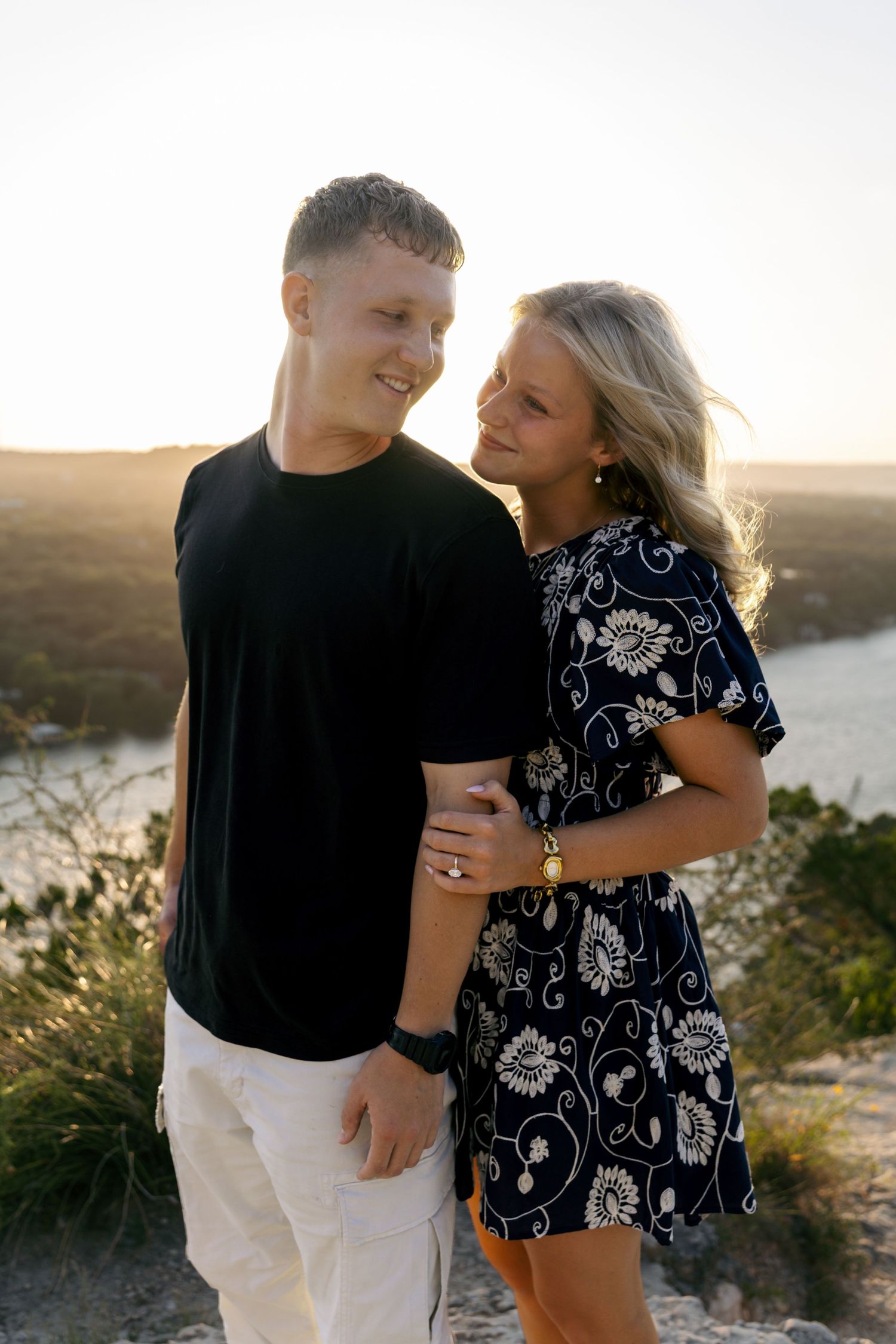 Young couple embracing at sunset on a rocky overlook with scenic landscape behind them.