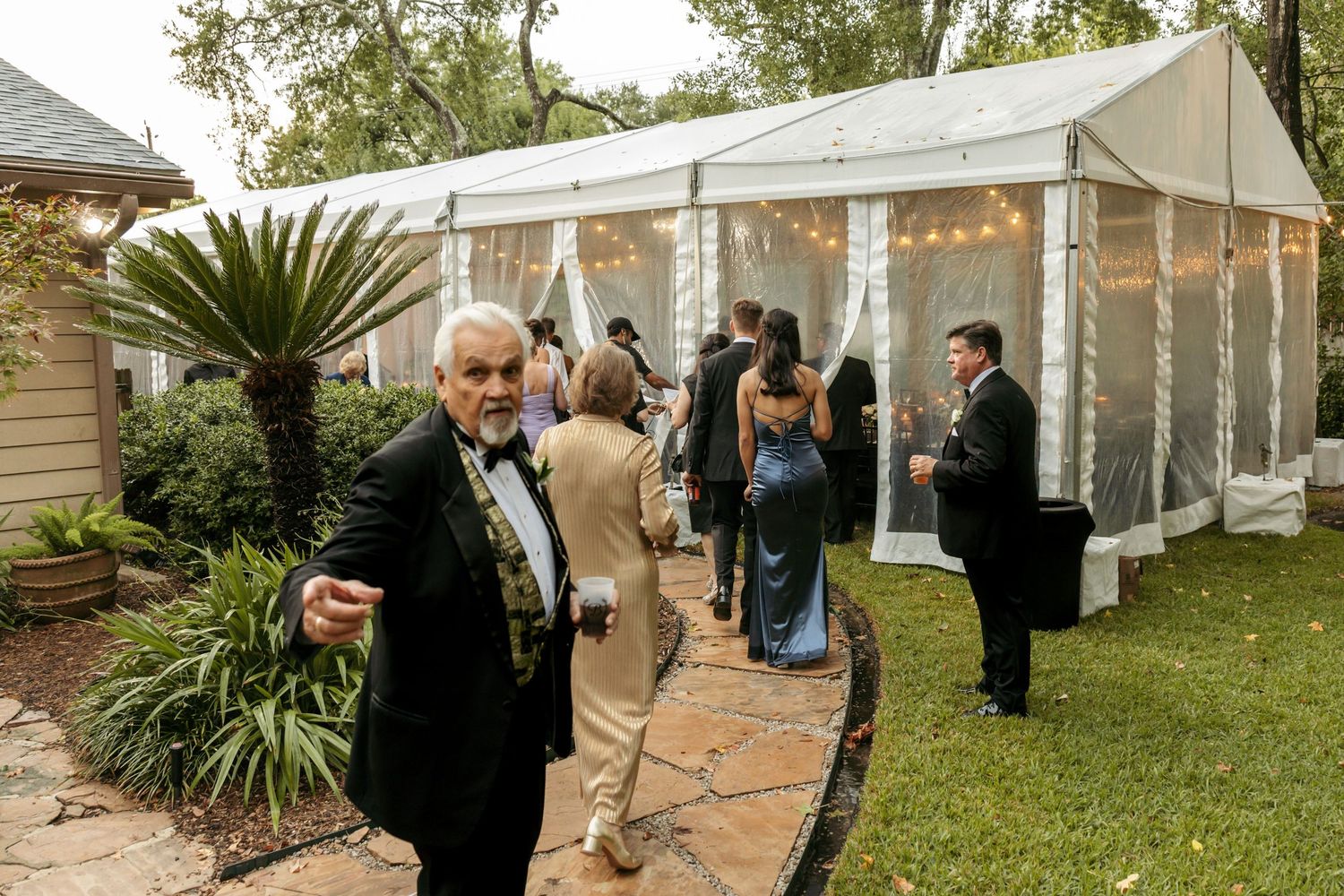 Wedding guests mingle outside a white tent with string lights at an elegant outdoor garden reception.
