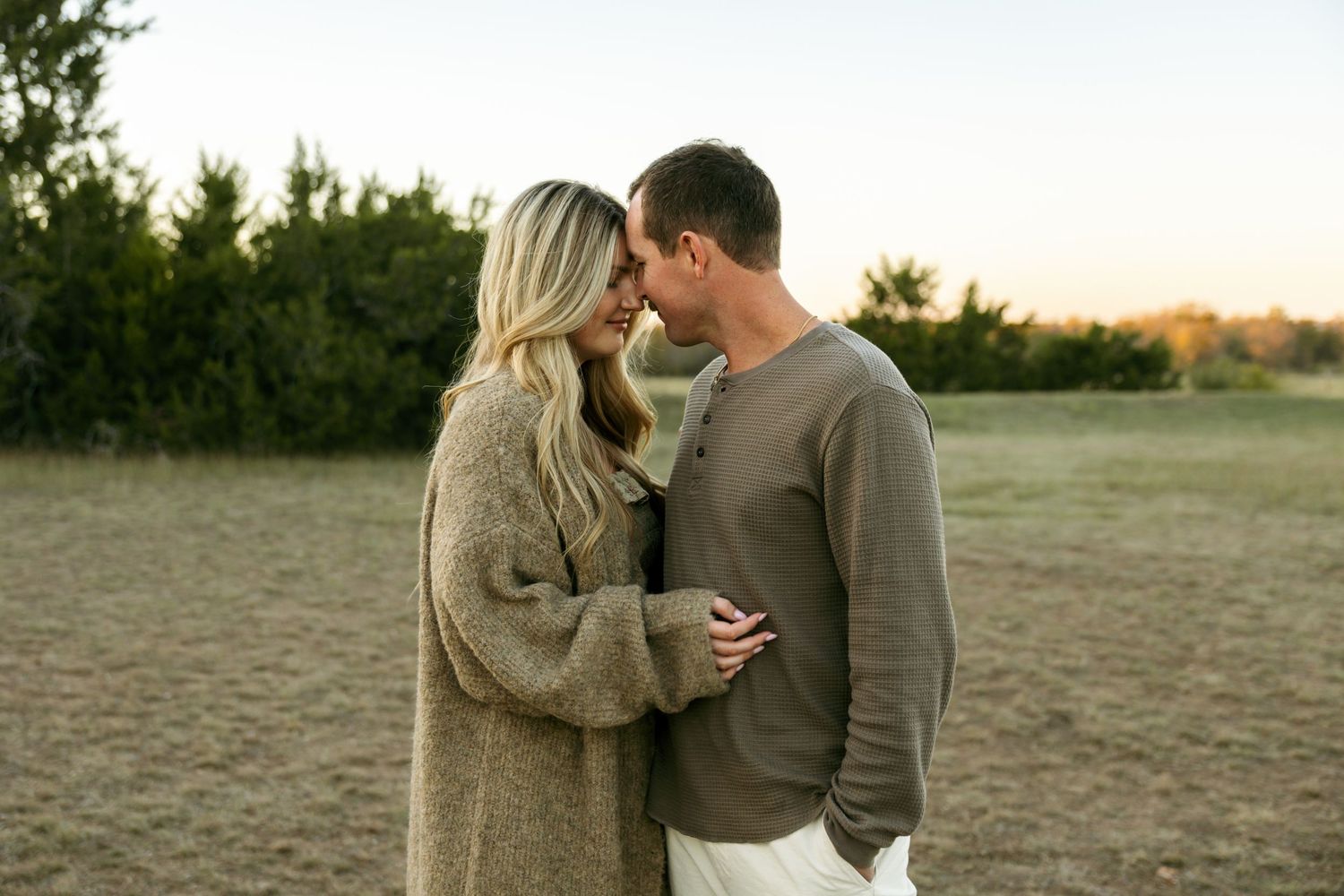 Couple touching foreheads romantically at golden hour in an open field.