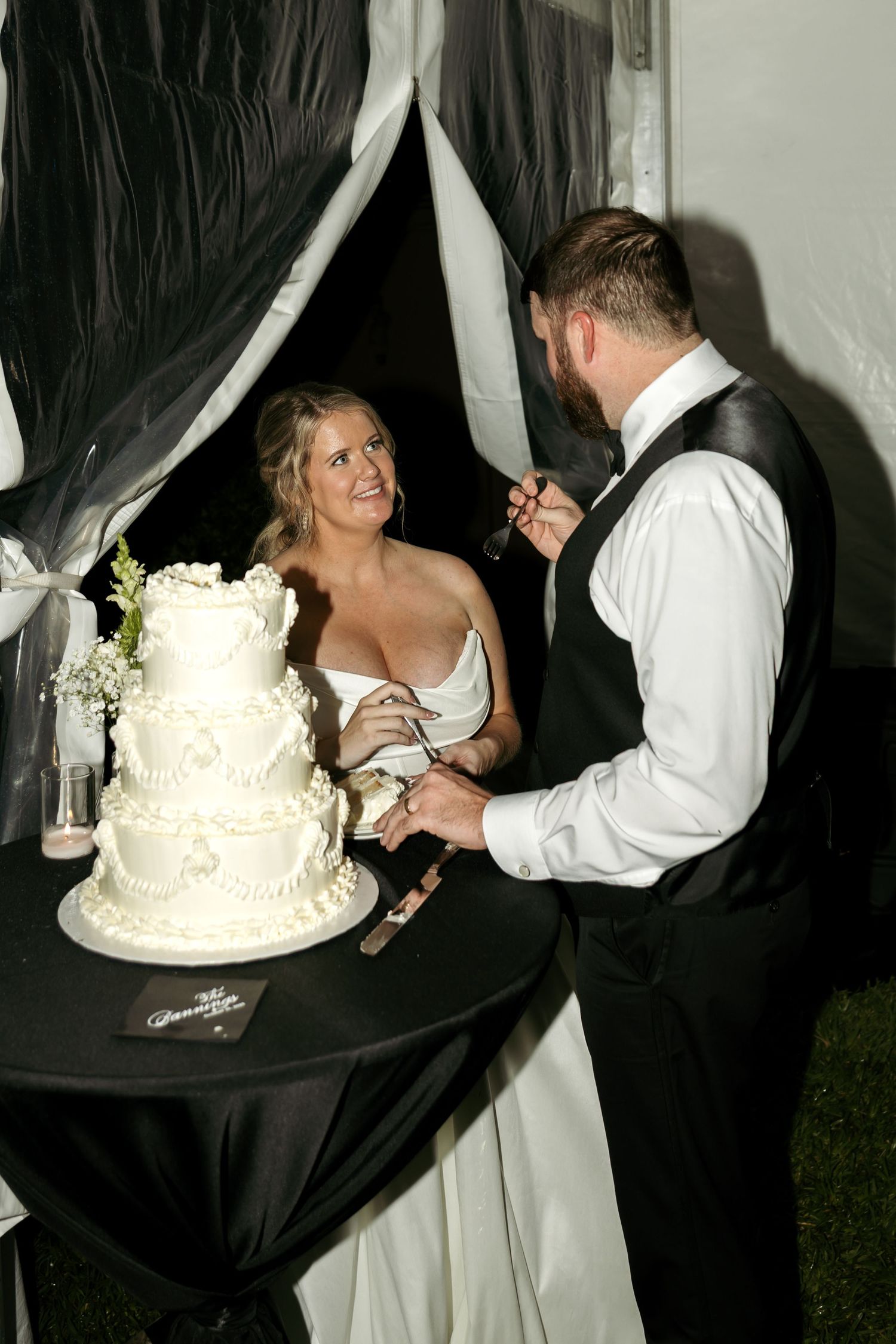 Bride and groom cutting their white tiered wedding cake together at a tented reception.