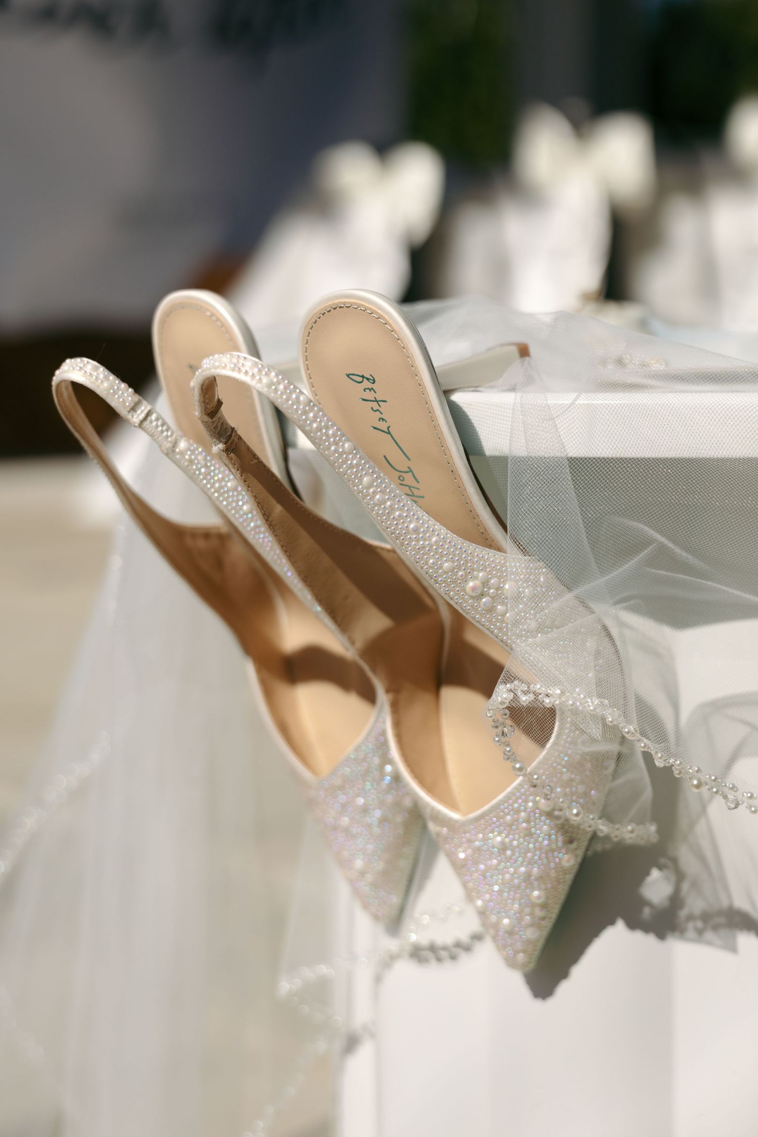 Sparkling crystal-embellished slingback bridal heels resting against white chair with tulle veil.