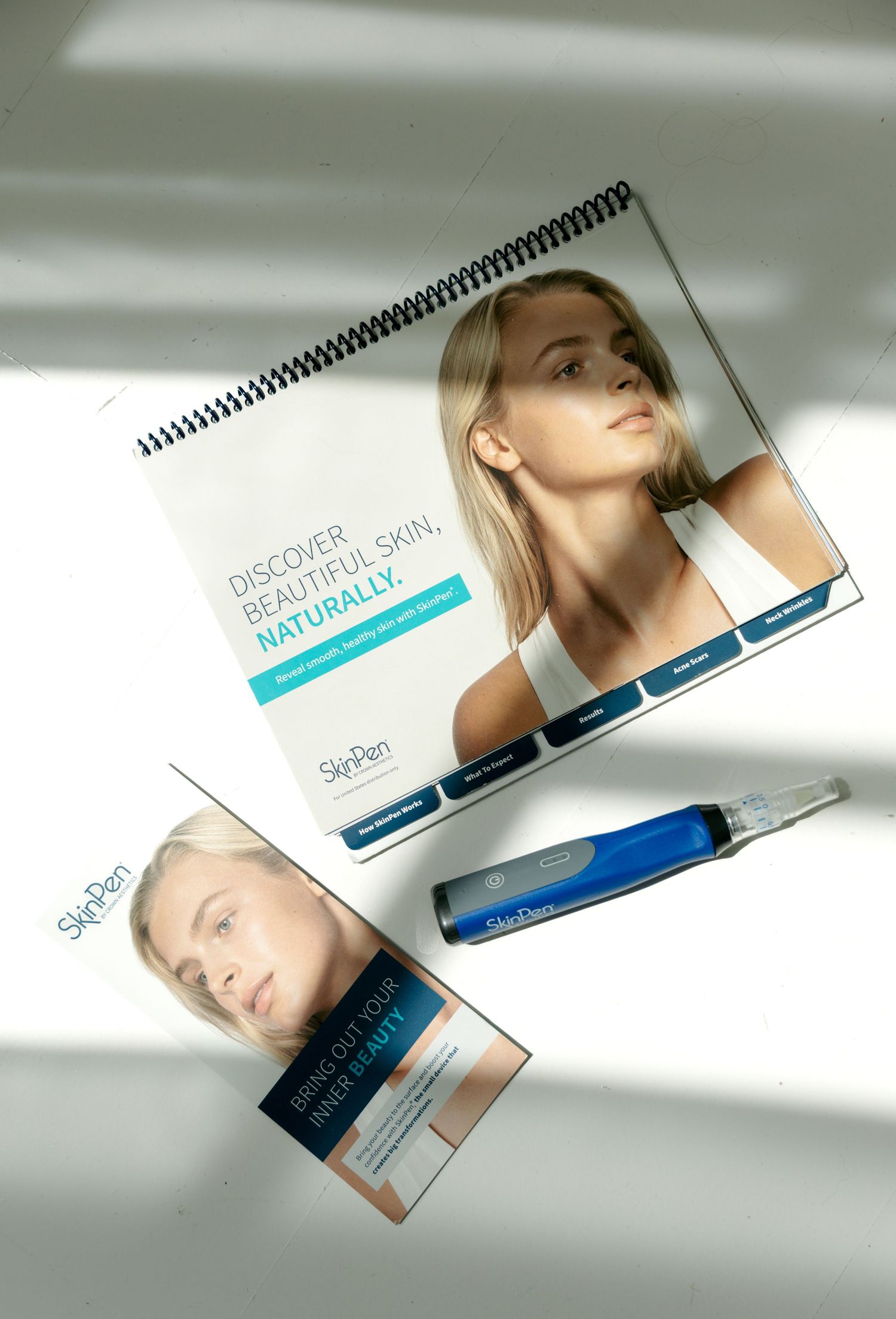 SkiPen microneedling device displayed with branded brochures and a spiral-bound beauty treatment guide.