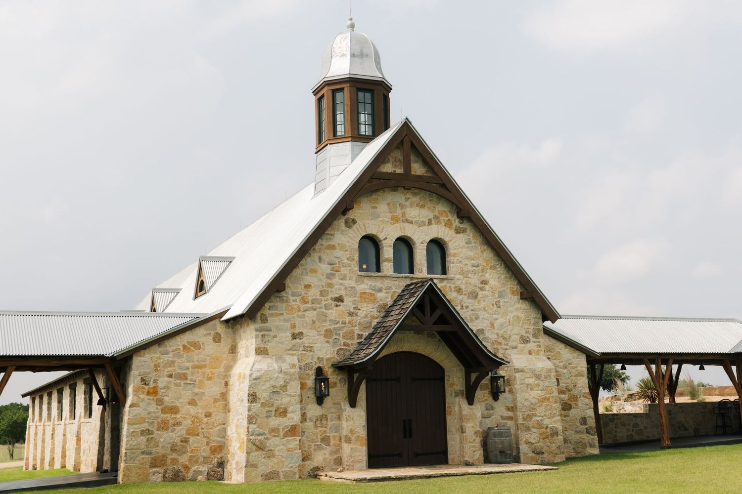 Rustic stone wedding chapel with wooden accents and metal roof under cloudy sky.
