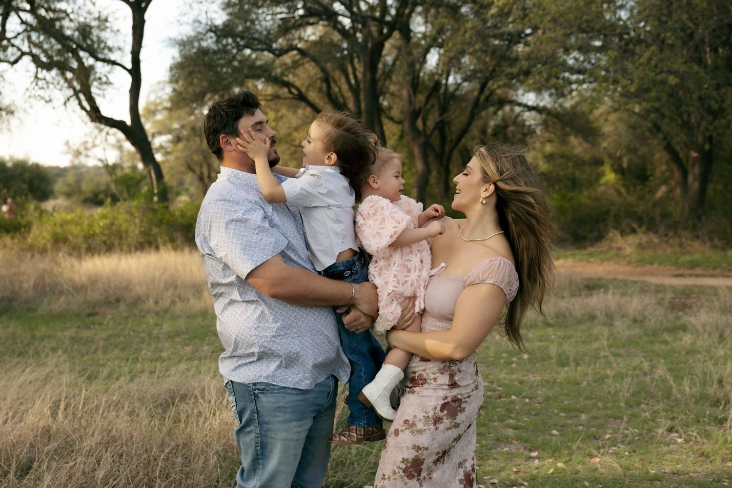 Joyful family moment outdoors with father holding toddler and mother cradling young child.