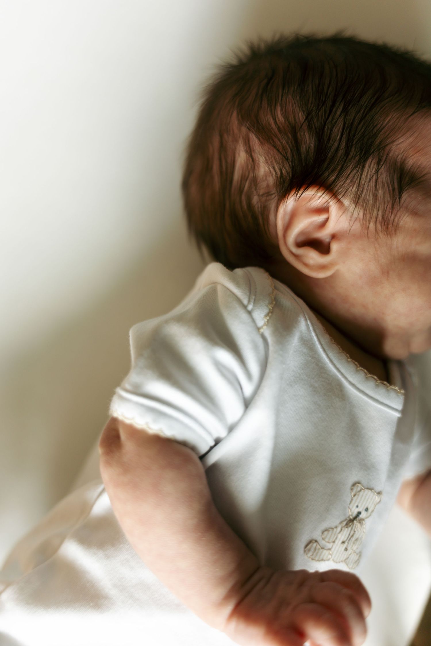 Close-up of a newborn baby with dark hair wearing a white bear onesie.