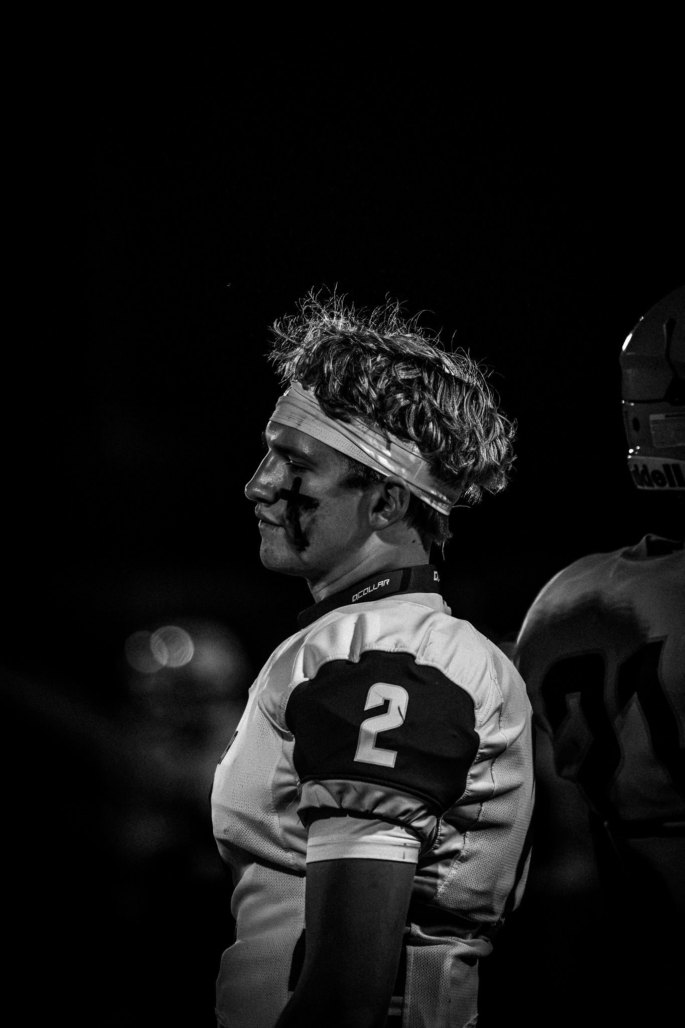 Black and white portrait of smiling football player wearing number 2 jersey and headband at night.