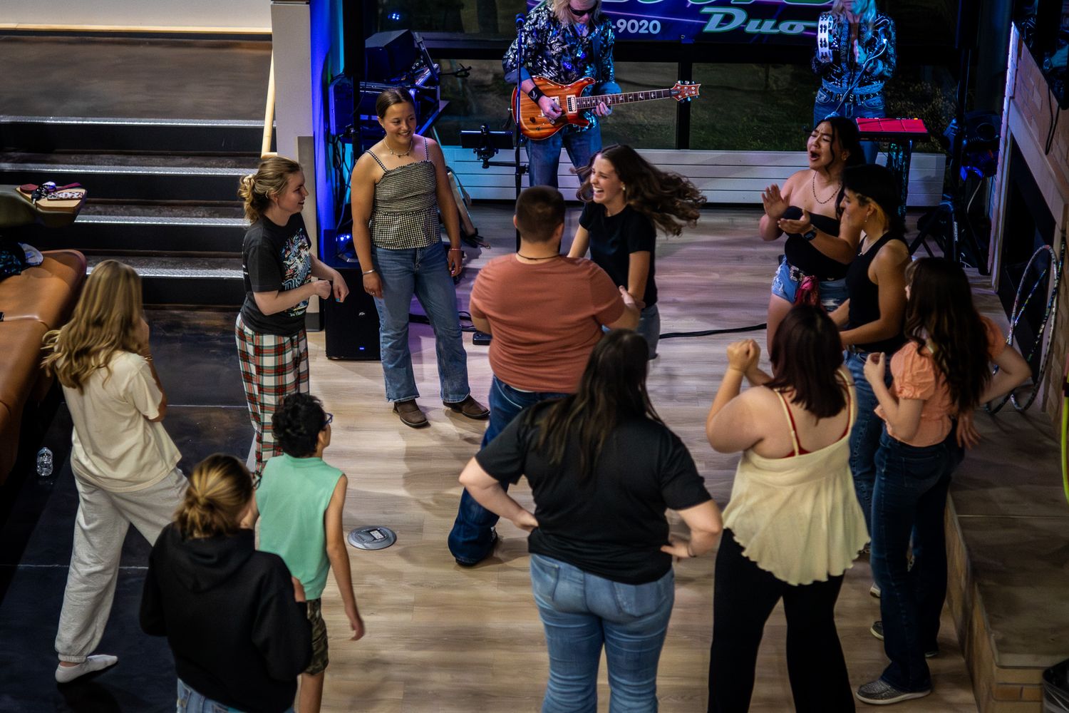 Group of people dancing together at a live music venue with a band performing on stage in the background.