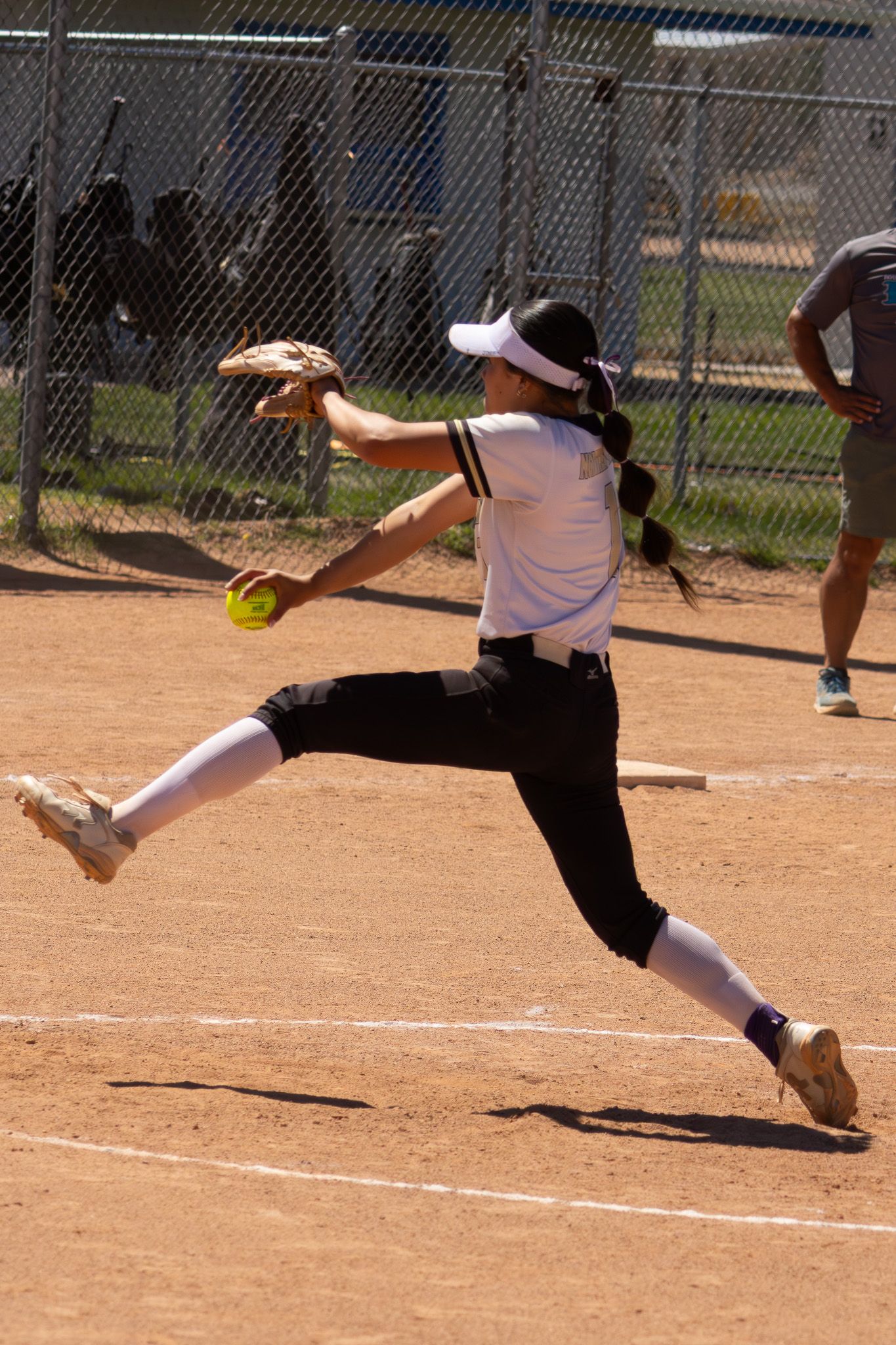 Female softball pitcher winds up for powerful underhand pitch on mound during game.