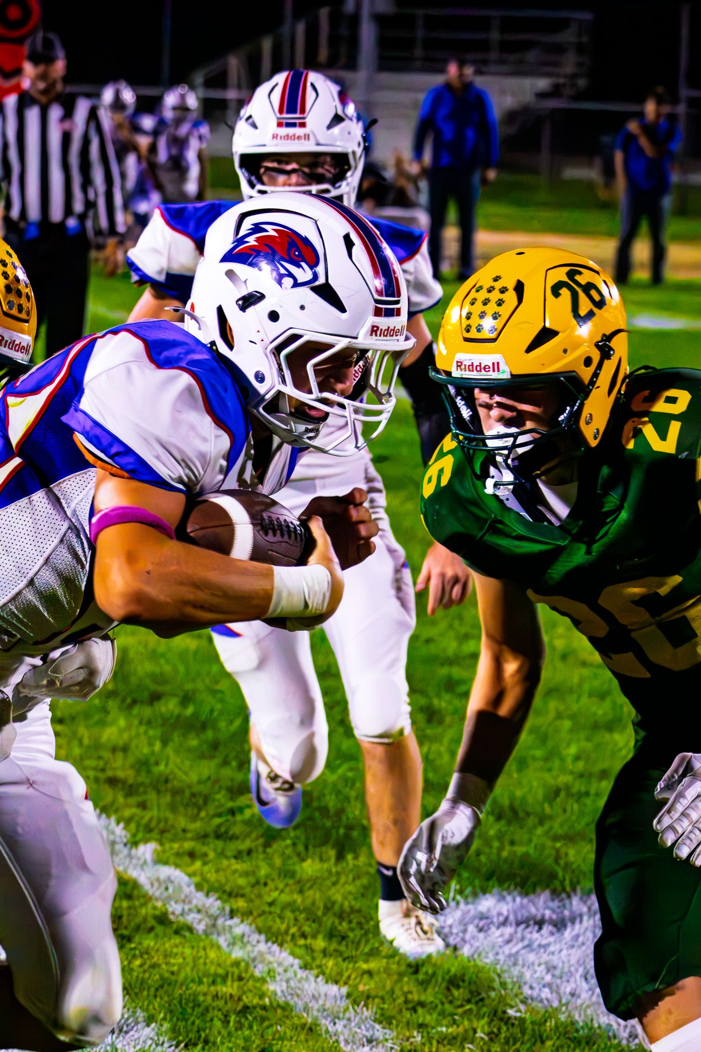 Blue and white football player runs with the ball as green and gold defender #26 moves in to tackle.