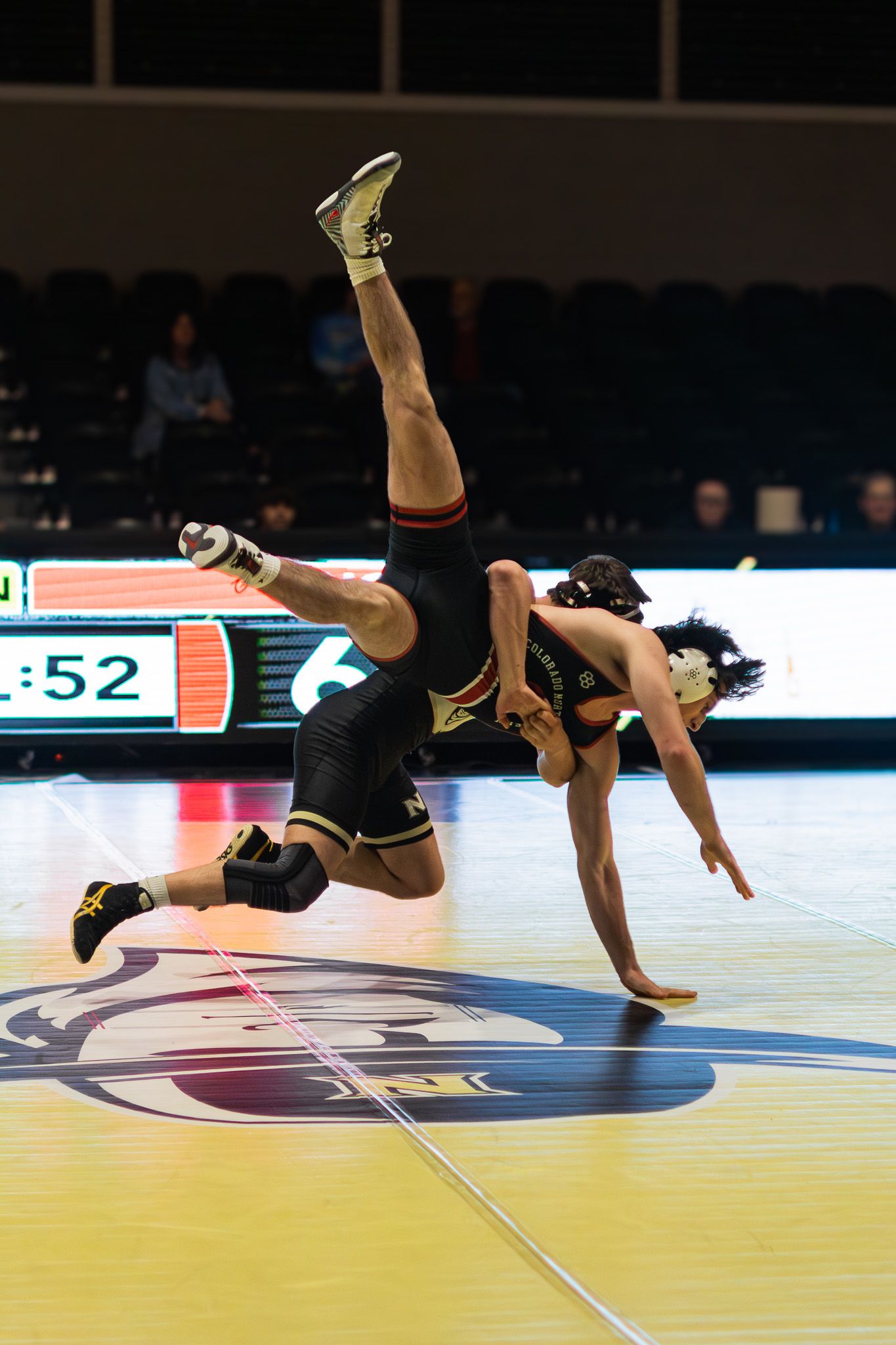 Dynamic wrestling throw with athlete airborne during competitive college wrestling match.