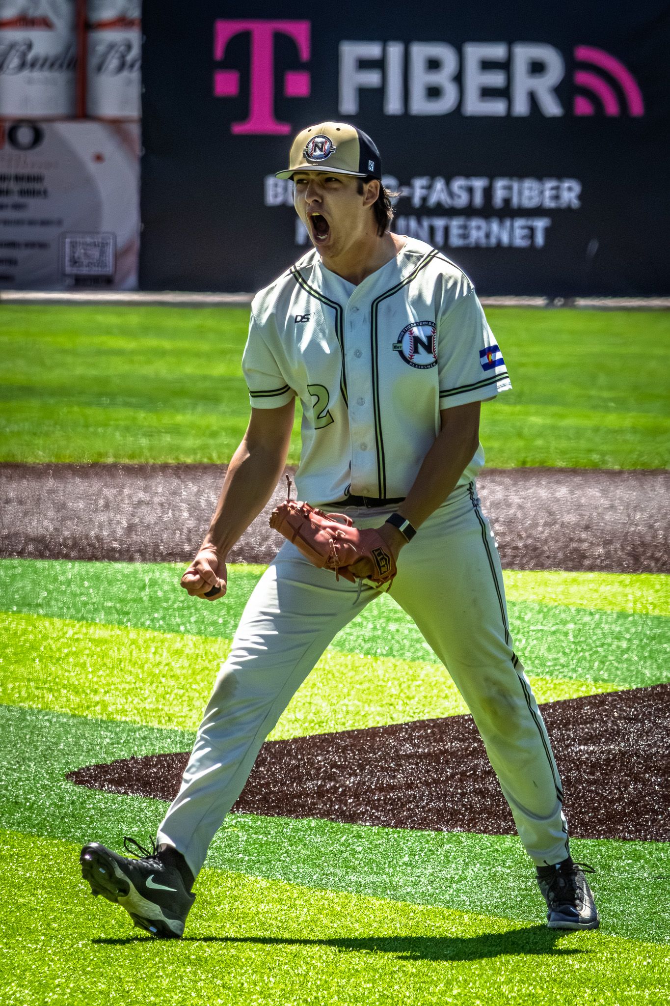 A baseball pitcher in white uniform celebrates with a fist pump on the mound after a successful play.