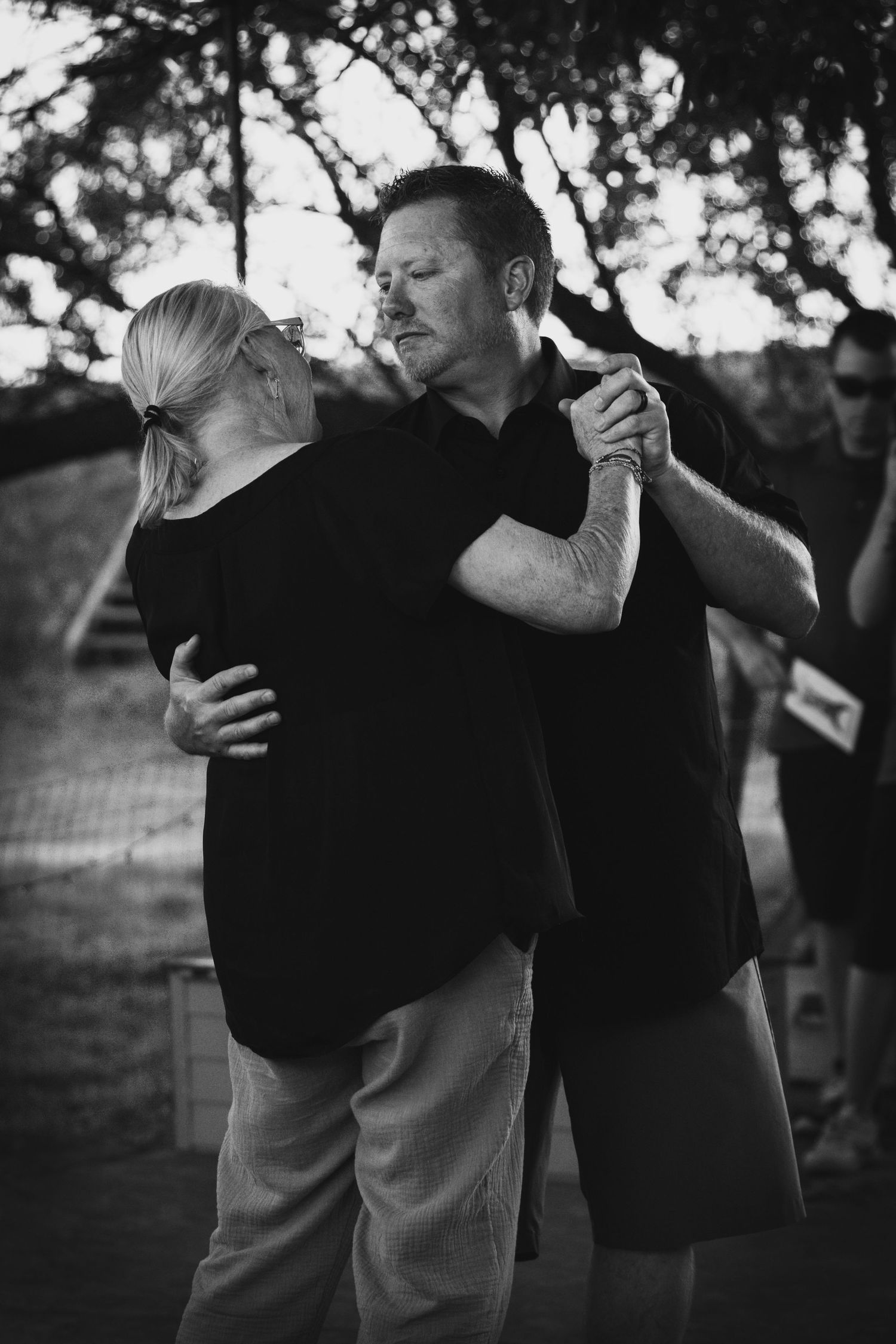 A couple slow dances closely together in a black and white outdoor photo taken at dusk.