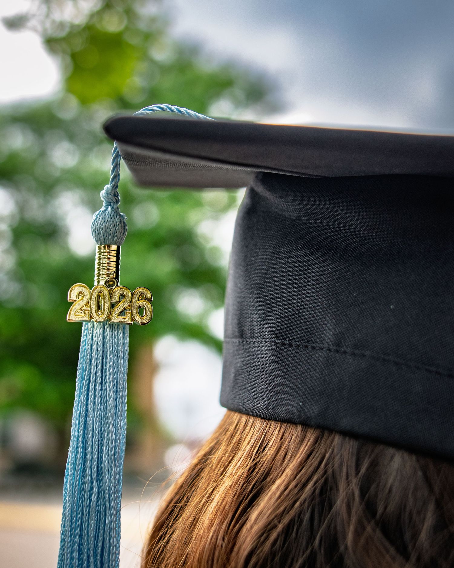 Close-up of a graduation cap with a teal tassel and gold 2026 charm on a student.