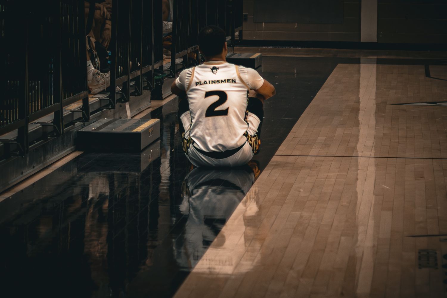 A Plainsmen player number 2 sits alone on the court floor in a moment of defeat after a basketball game.