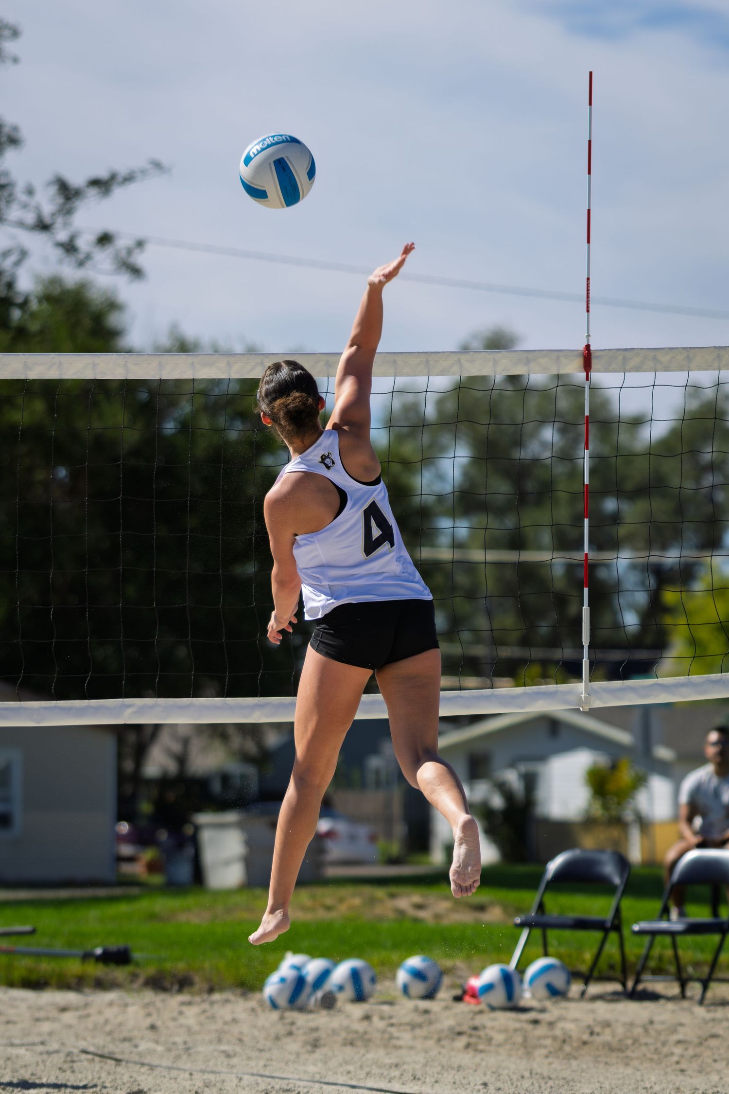 Female volleyball player wearing number 4 jumps to spike the ball over the net on a sand court.
