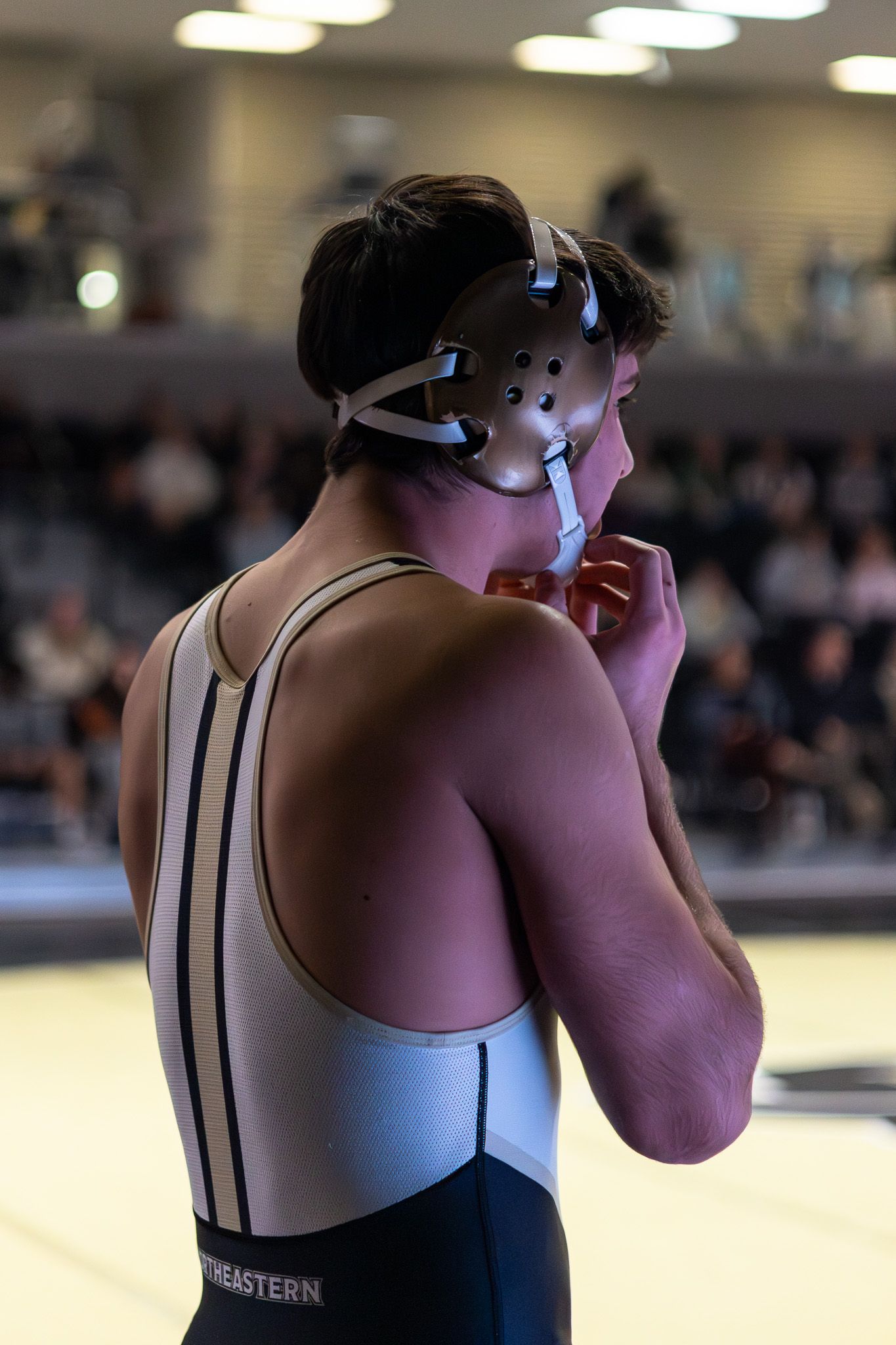 Close-up rear view of wrestler in Northeastern singlet adjusting headgear before match.