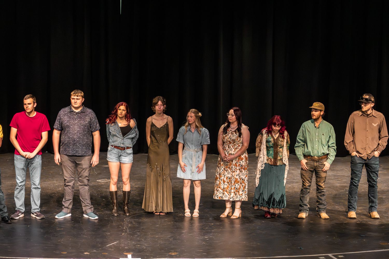 Group of nine students take a bow together on a dark theater stage after a performance.