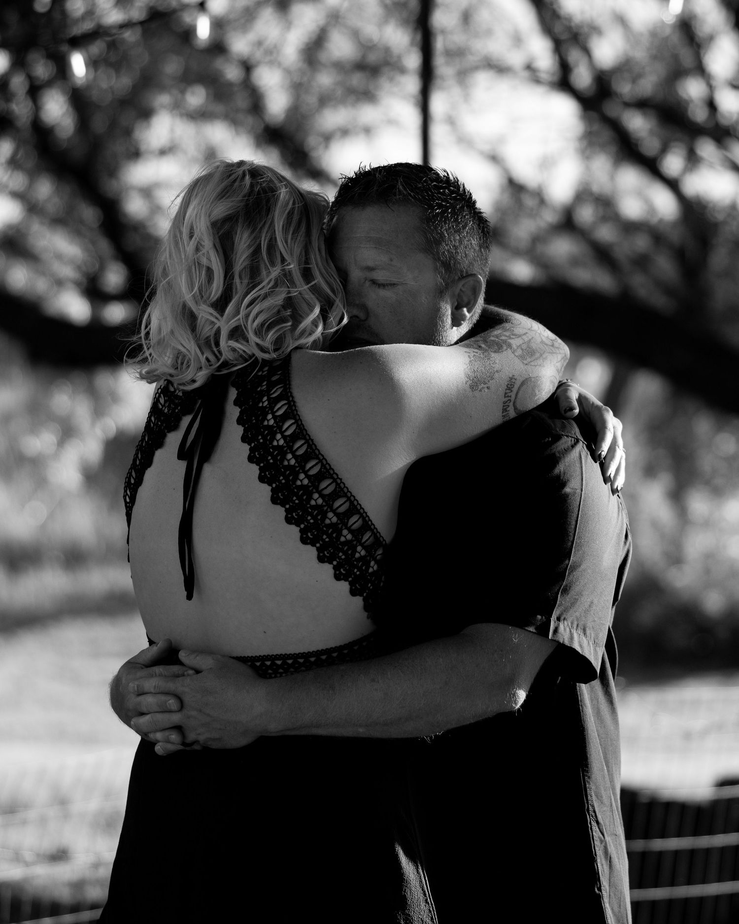 Black and white intimate photo of couple sharing a close embrace under a tree.