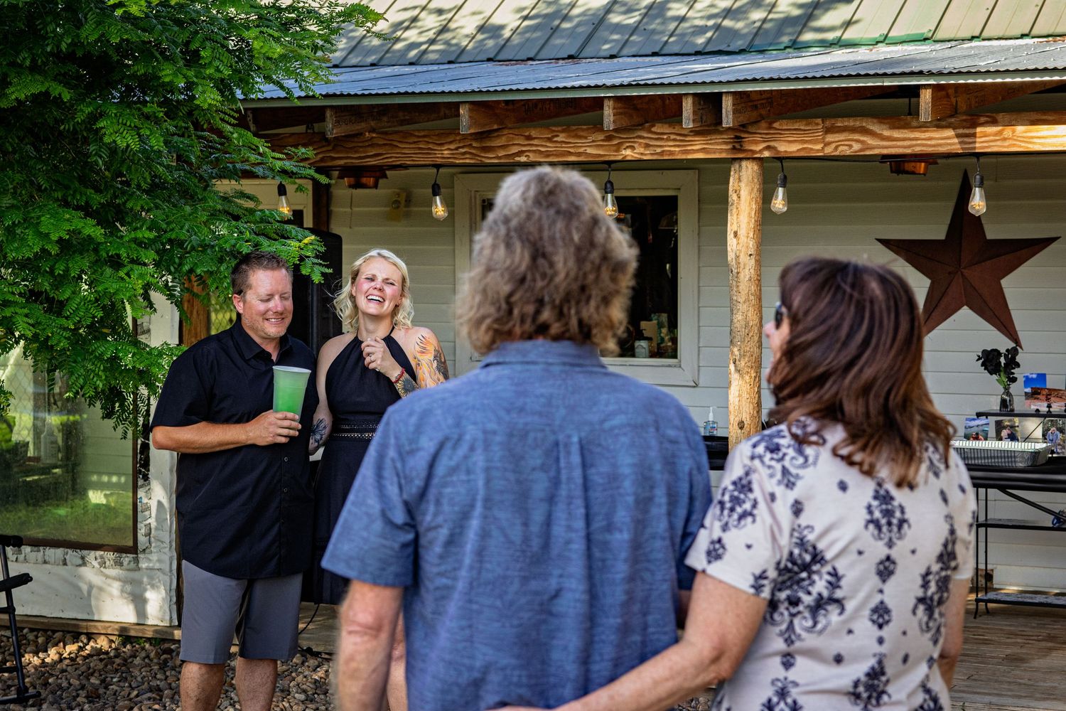 Group of people socializing outside a rustic wooden porch with a decorative metal star during an outdoor gathering.