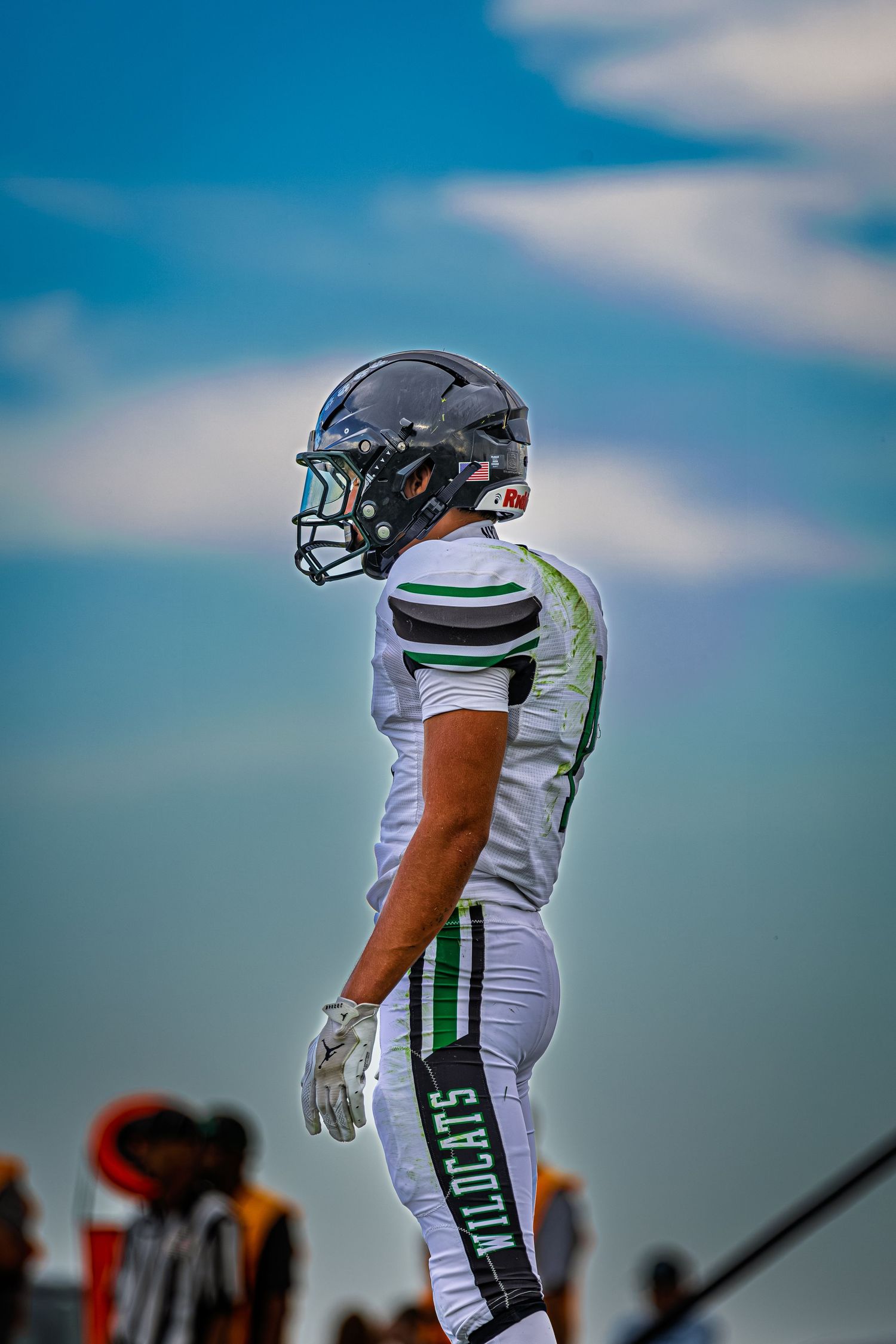 A Wildcats football player in white and green uniform poses against a blue sky backdrop.