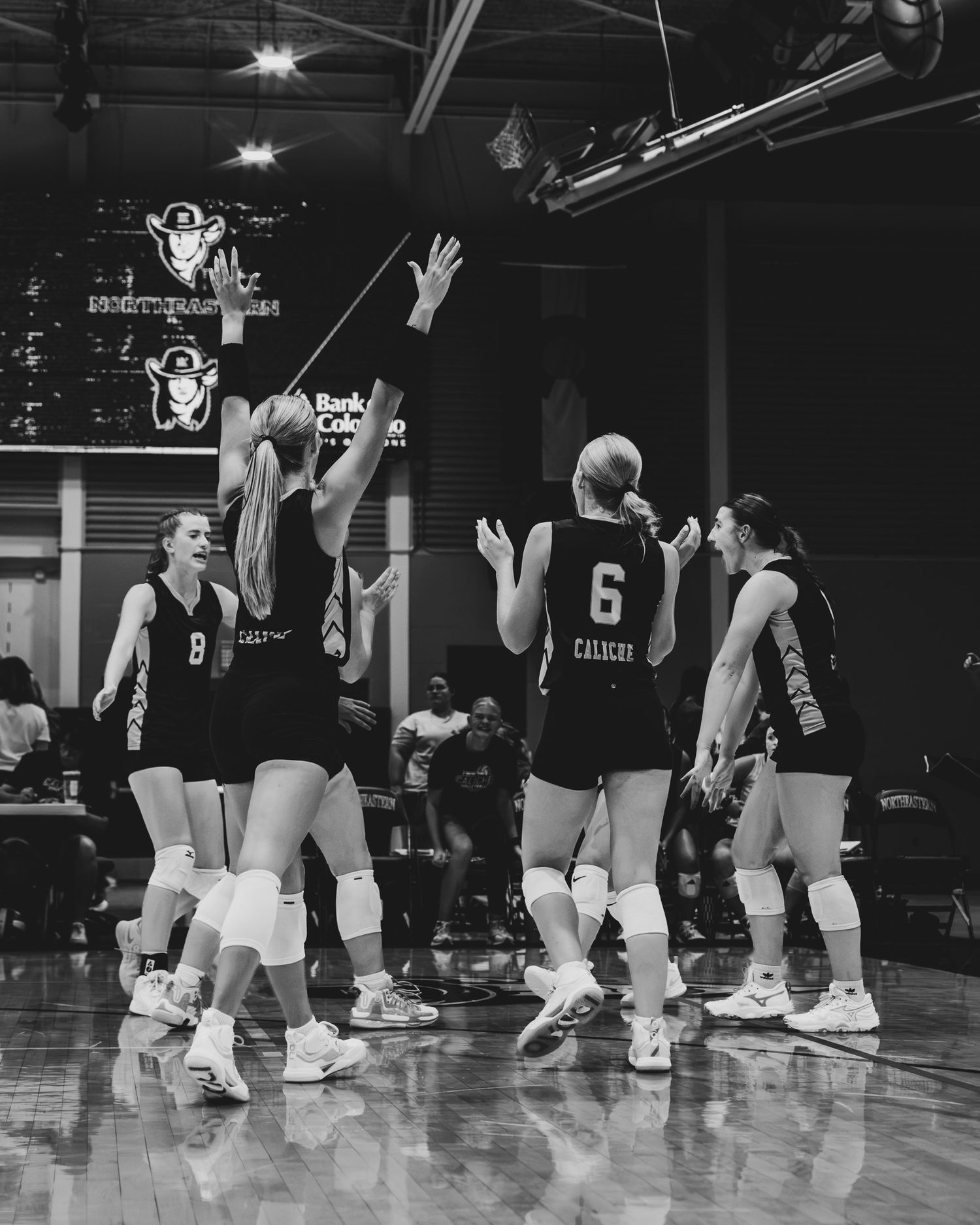 Calvary volleyball team huddles together on court during indoor match in black and white photo.