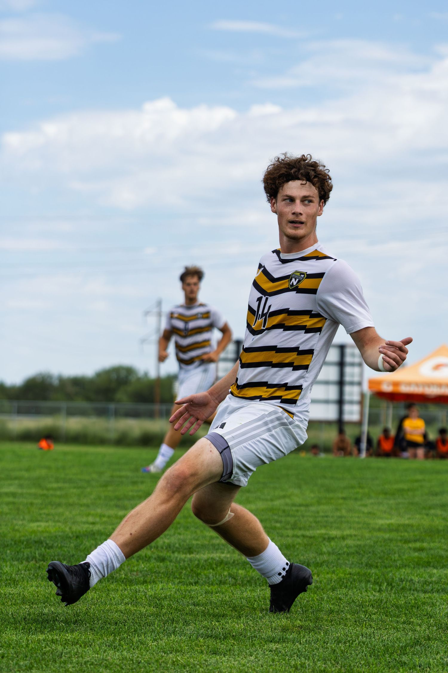 Young male soccer player in striped gold and white jersey sprints across a green grass field.