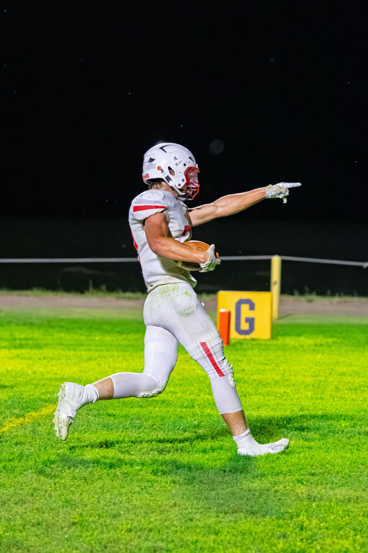 Football player in white uniform pointing while running on a green field during a night game.