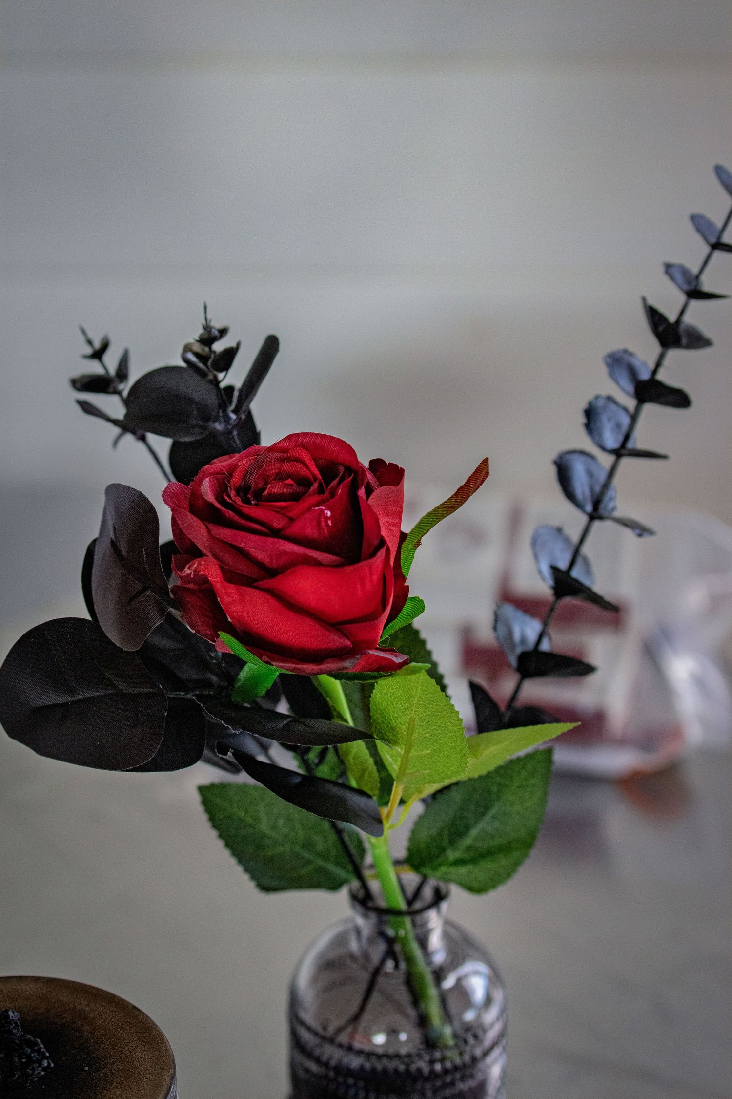 Single red rose with dark foliage in a small glass vase as elegant table decor against a soft background.