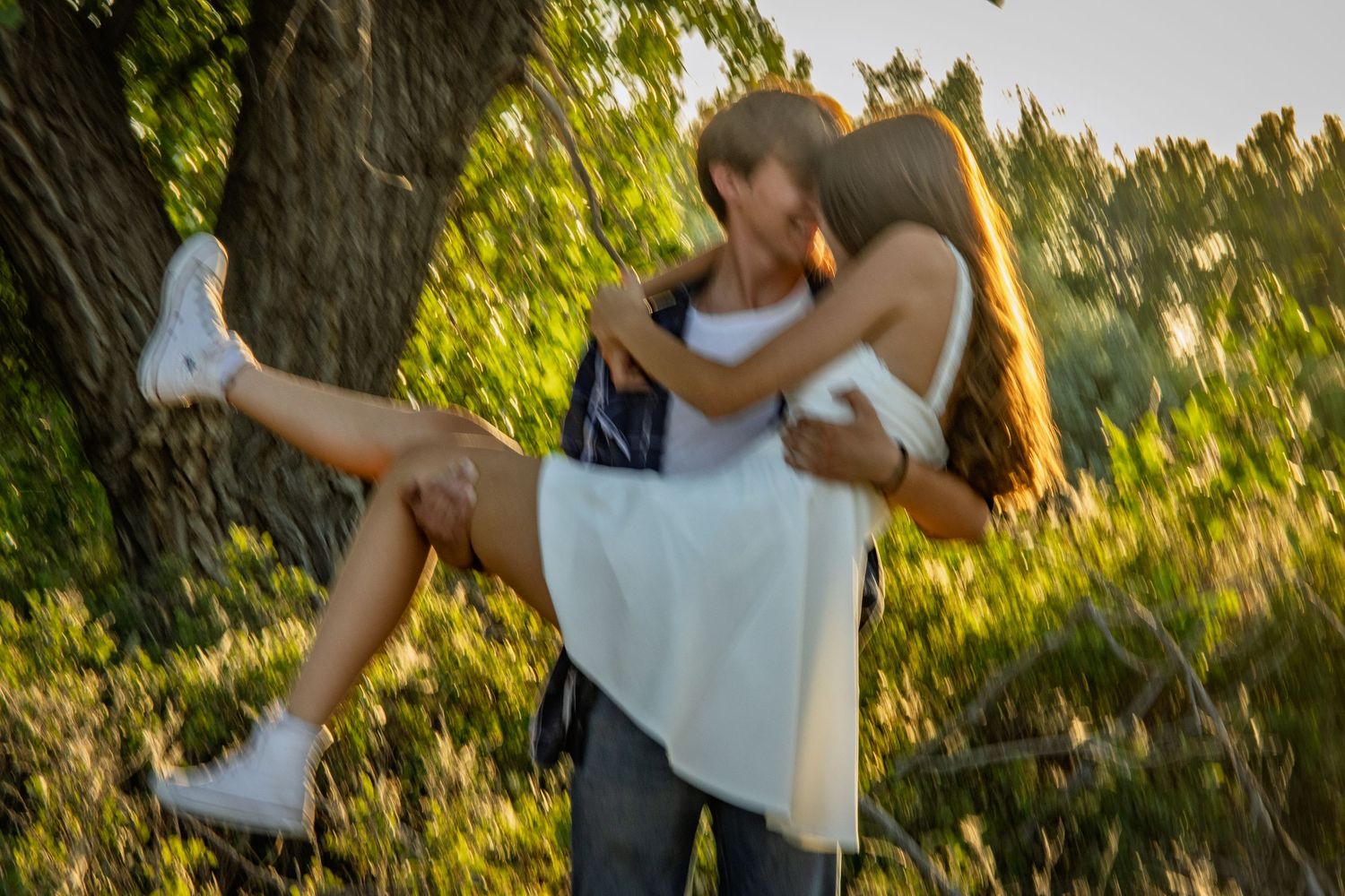 Young couple embracing and spinning together in a sunny green forest setting.