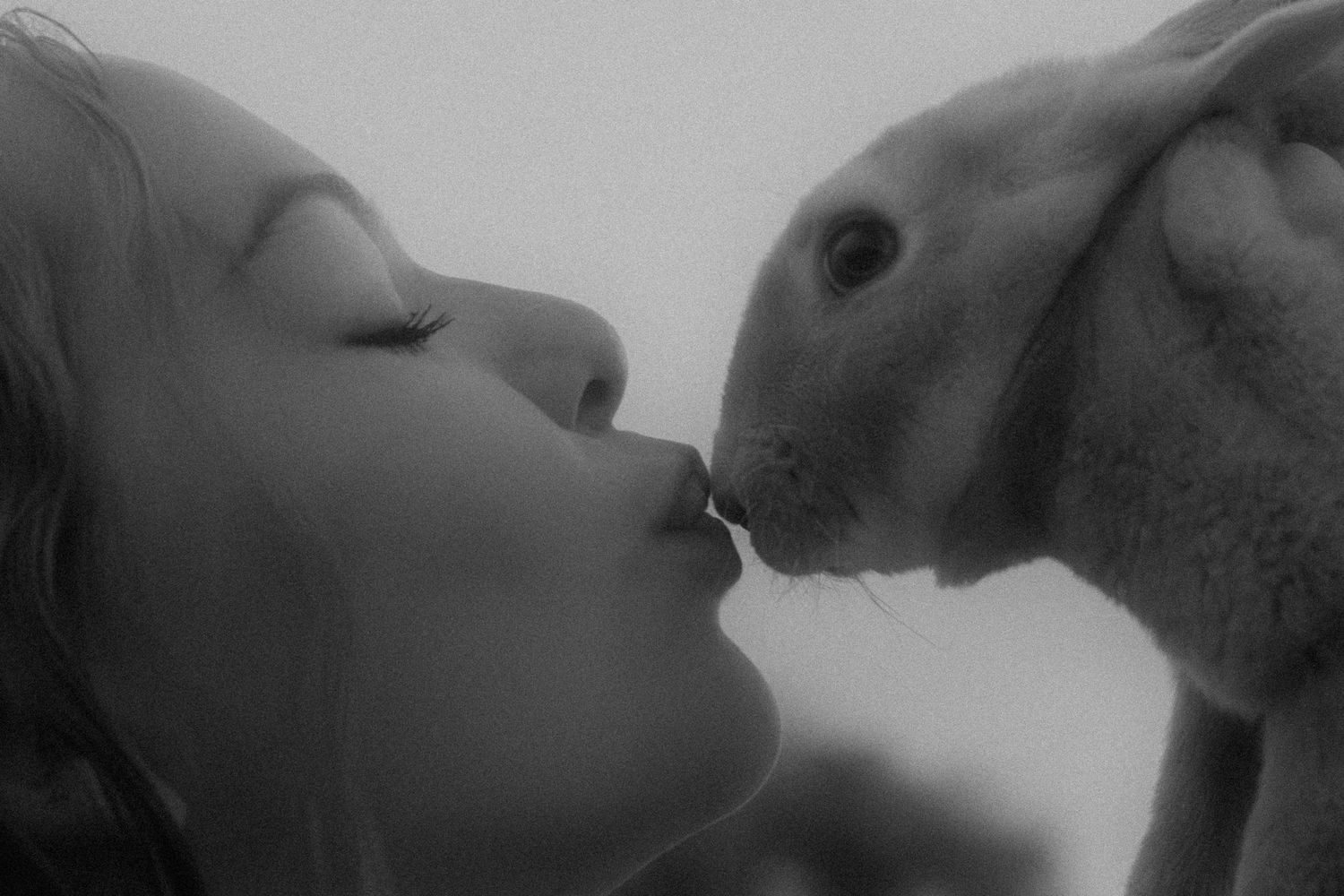 Black and white photo of a child gently touching noses with a small rabbit in a tender moment.