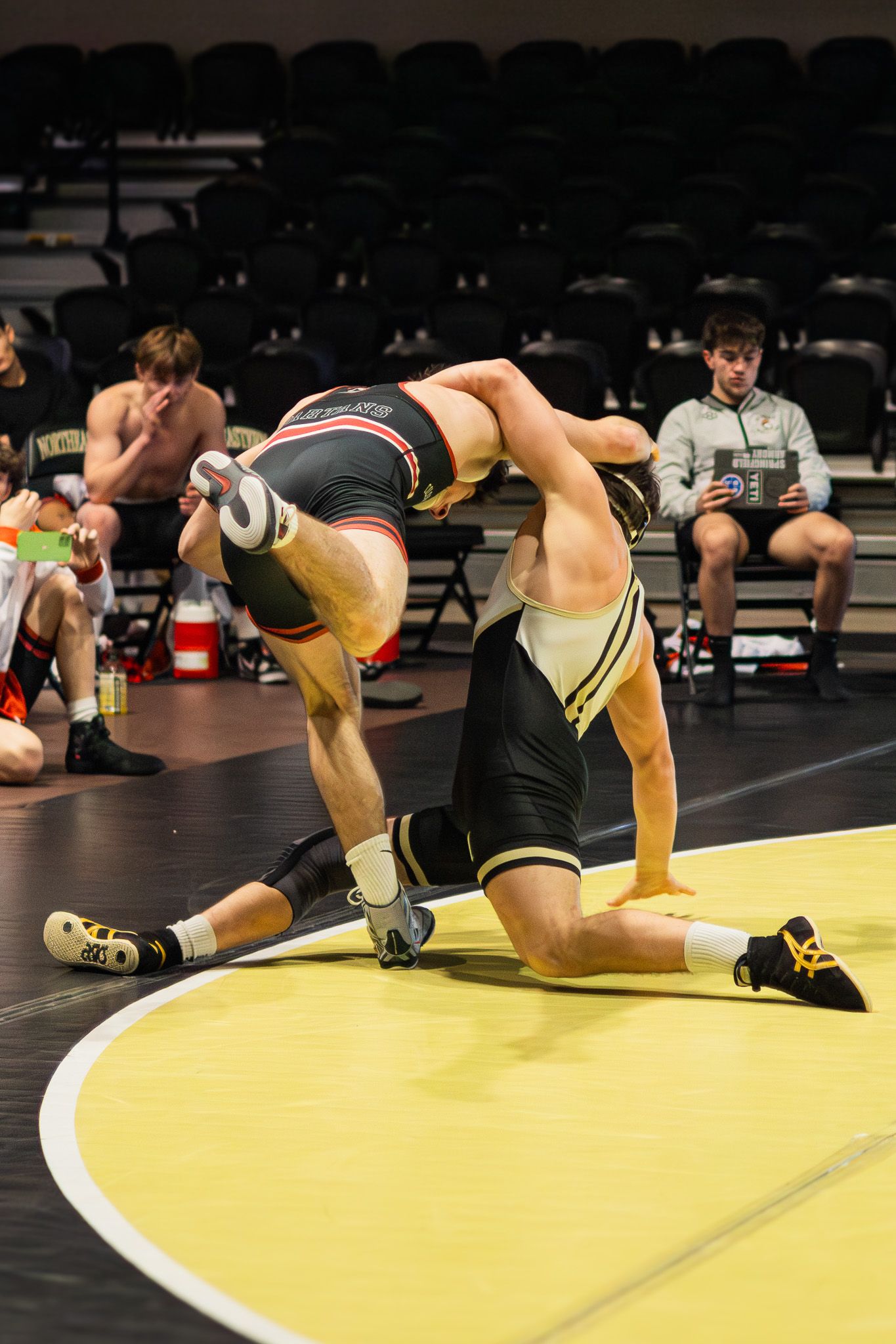 Wrestler in black singlet executes takedown on opponent during competitive wrestling match.