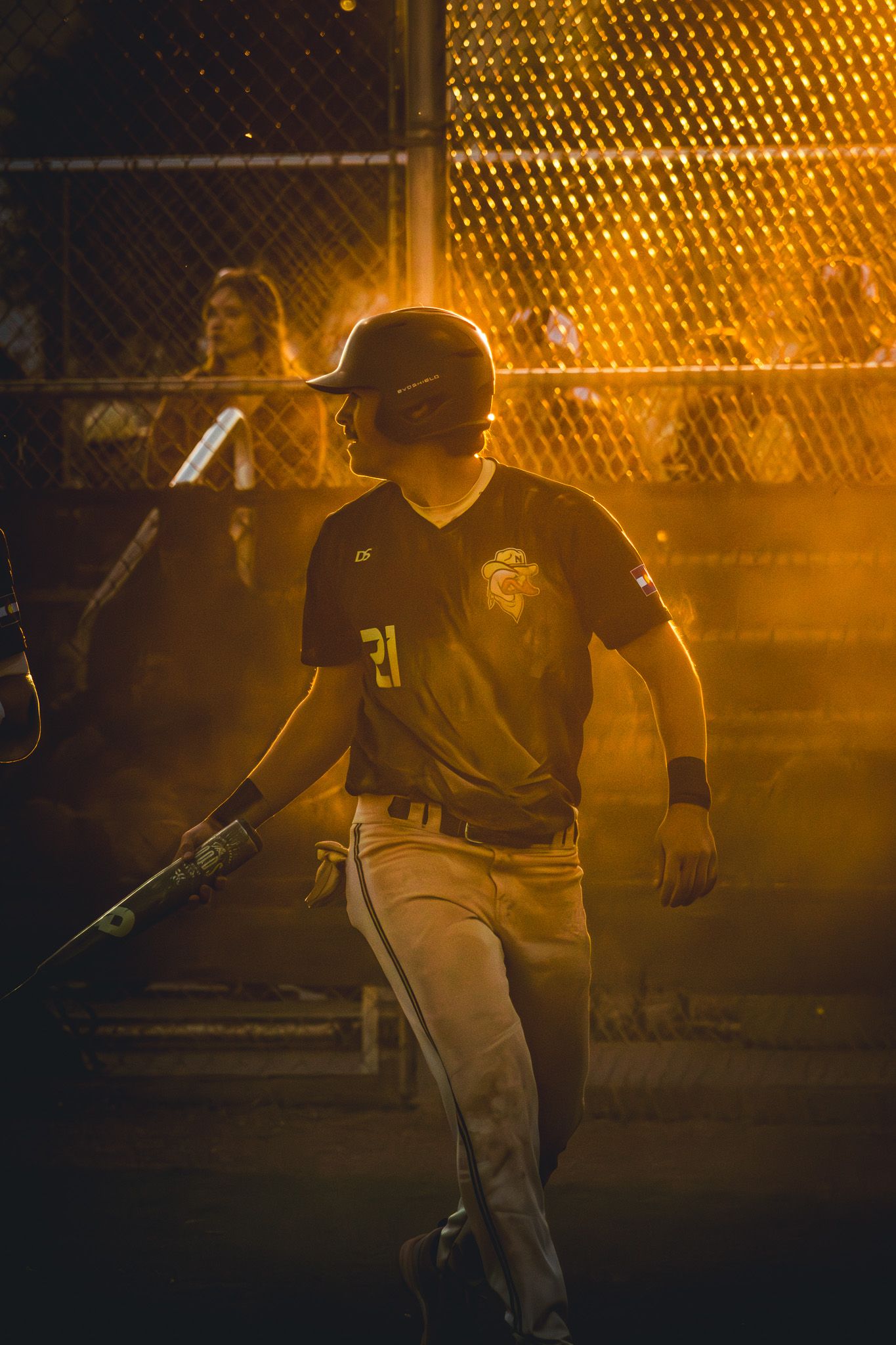 Baseball player number 21 holds a bat while bathed in warm golden light during a night game.
