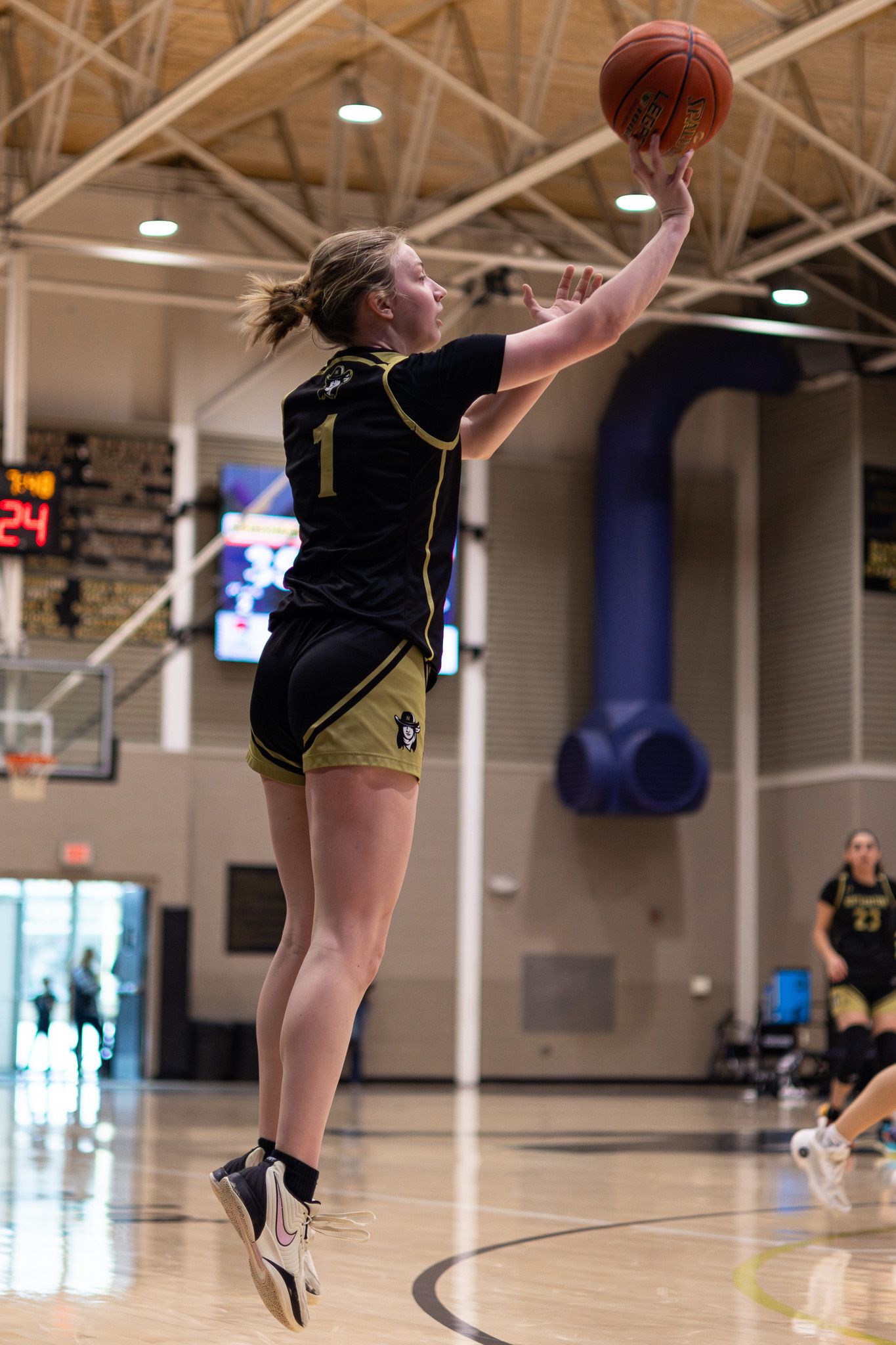 Female basketball player in black uniform number 1 leaps to shoot the ball during an indoor game.