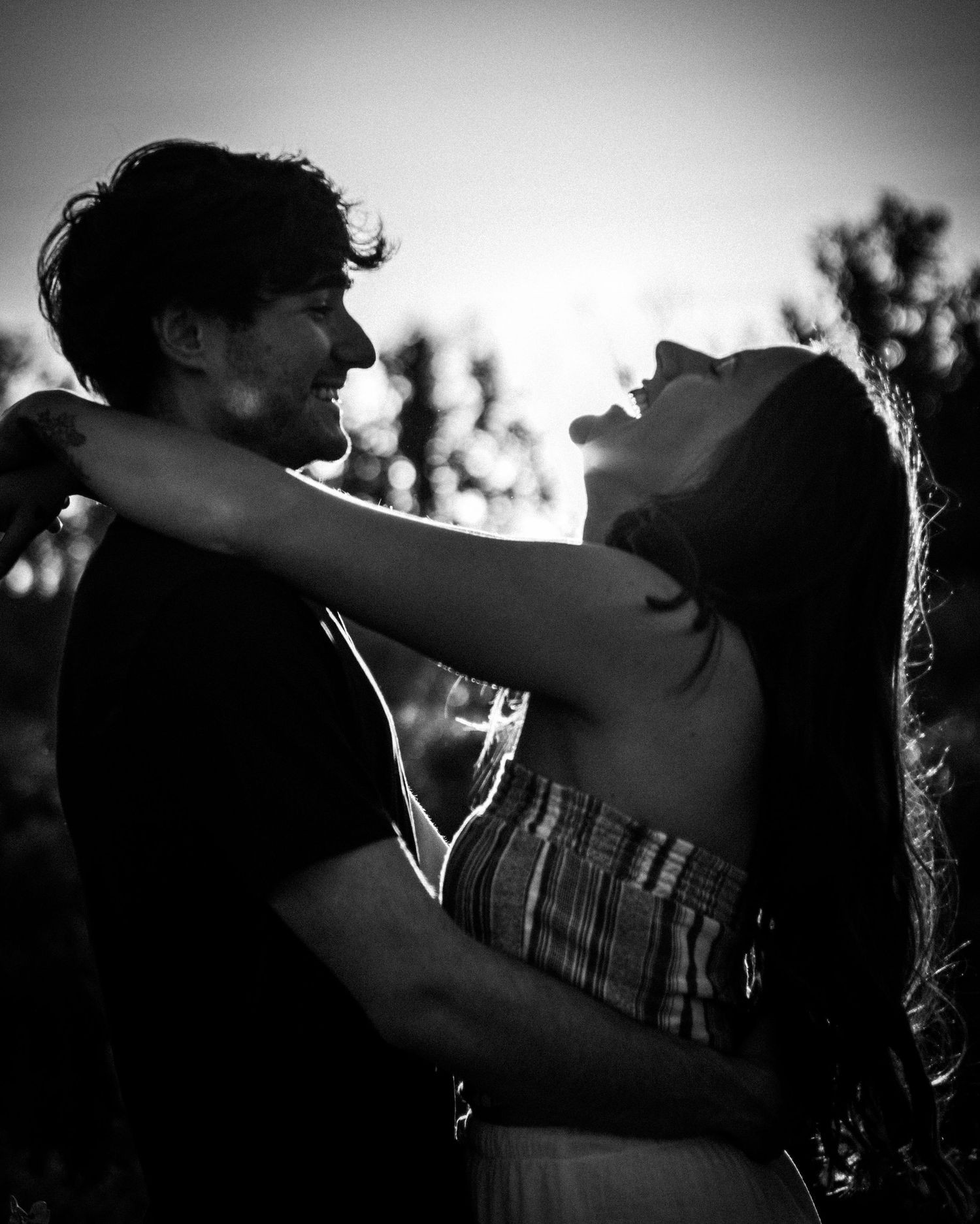Black and white romantic portrait of young couple embracing and laughing at sunset outdoors.