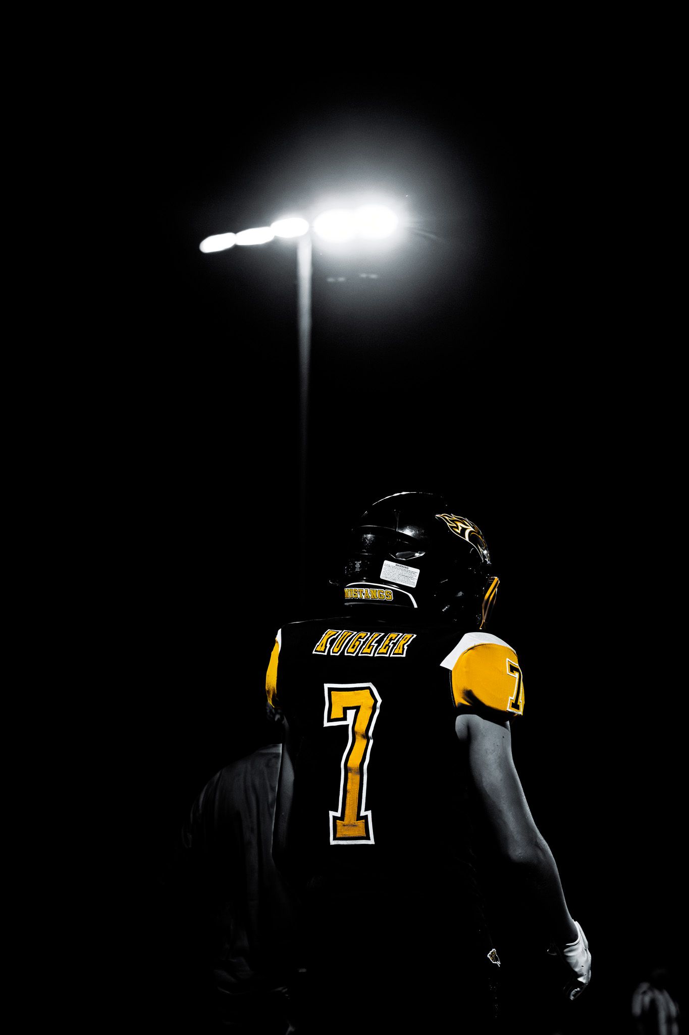 Football player wearing jersey number 7 stands under bright stadium lights in dramatic dark setting.