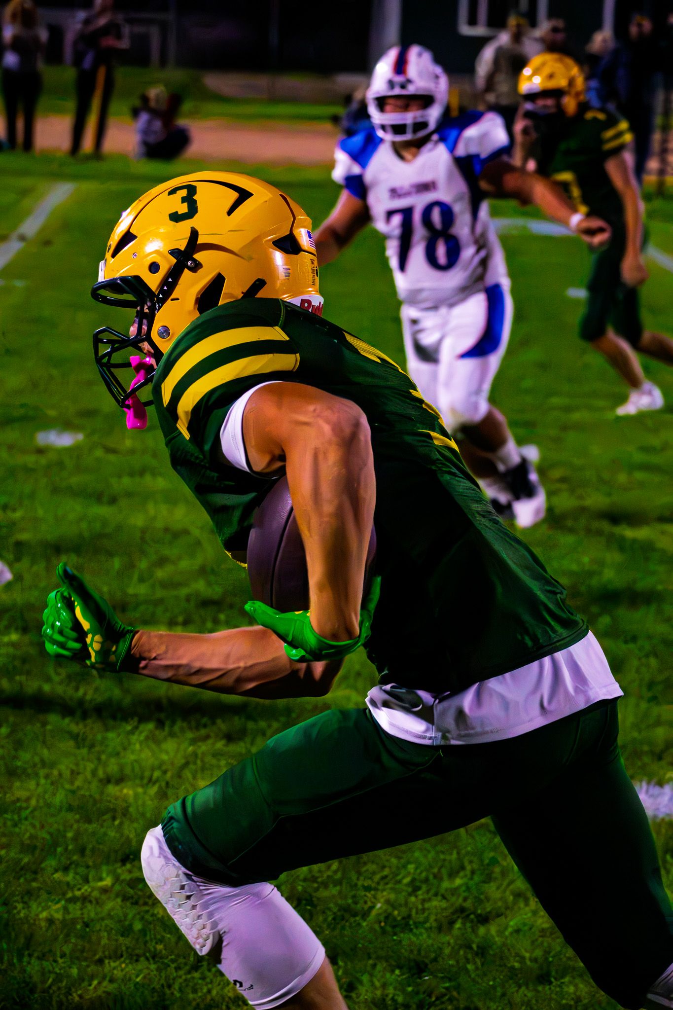 Football player #37 in green and gold uniform carries the ball during a night game.