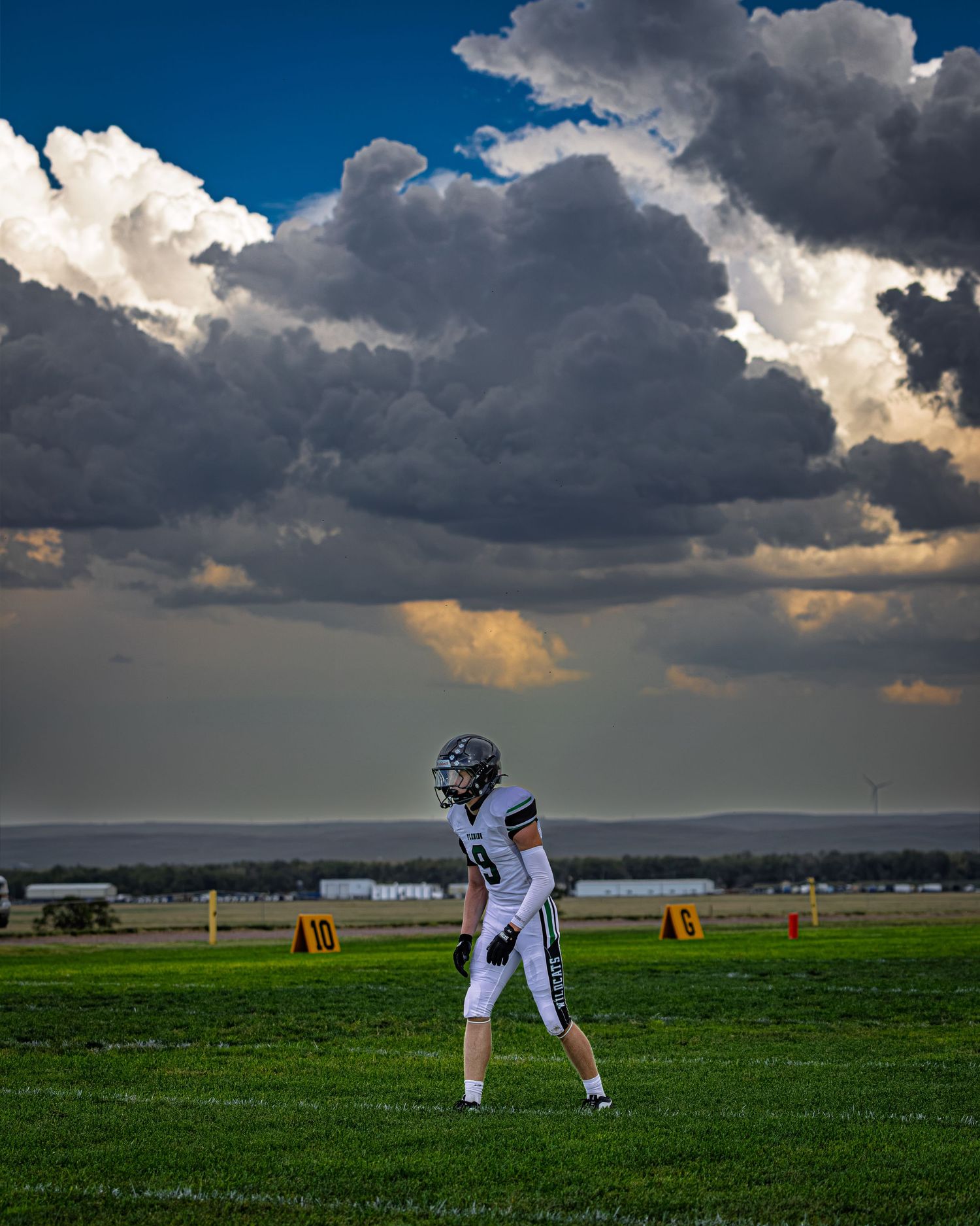 A lone football player stands on a green field beneath dramatic storm clouds and golden sunlight.