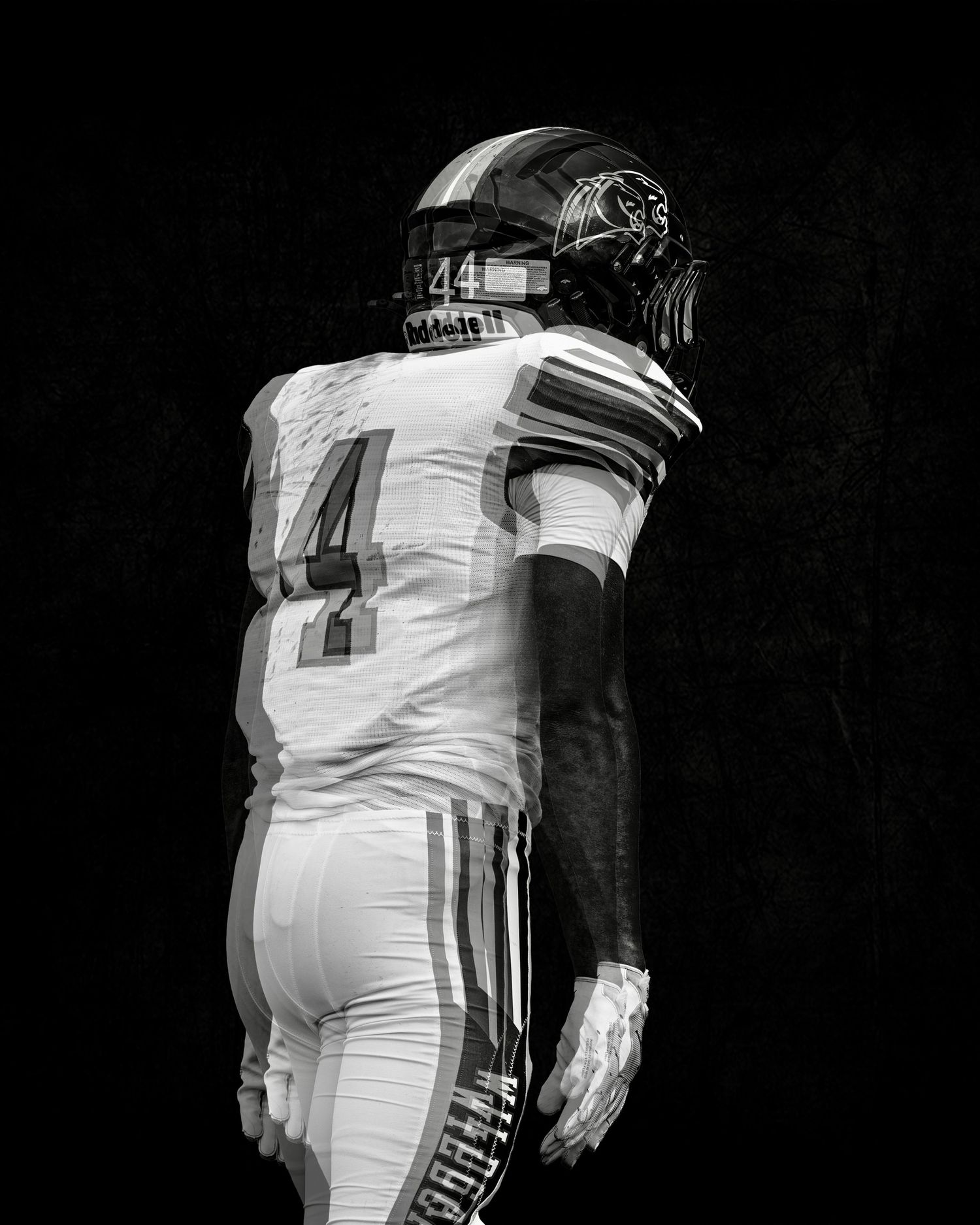 Black and white dramatic portrait of football player #44 in white uniform standing against dark background.