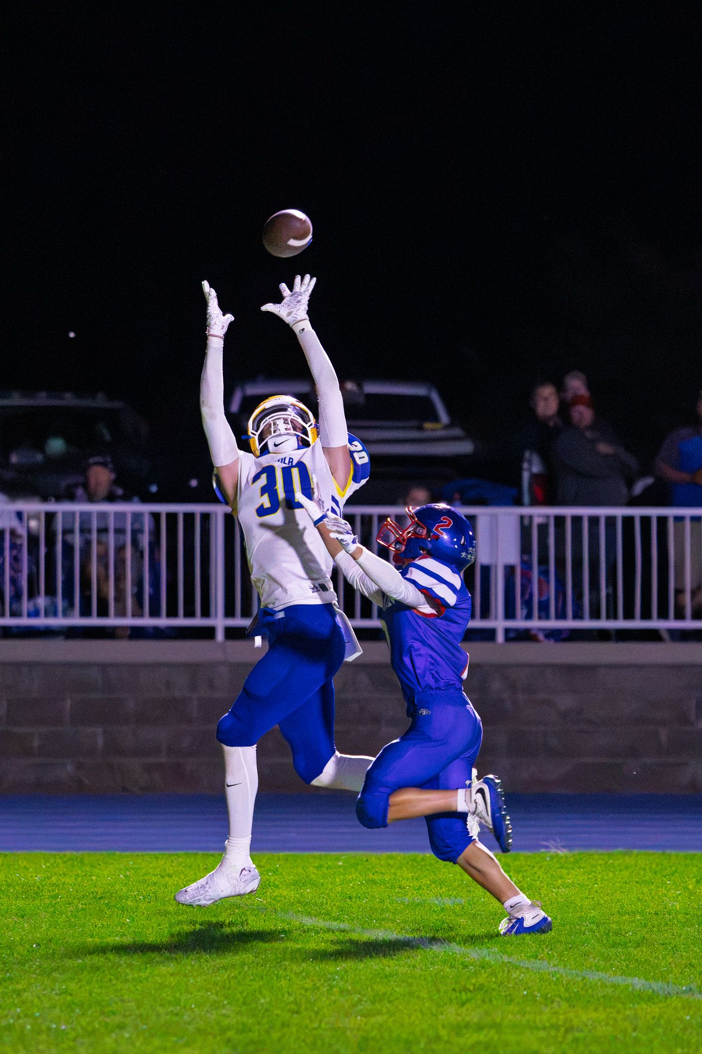 Football player number 30 leaps to intercept pass over defender during night game action.